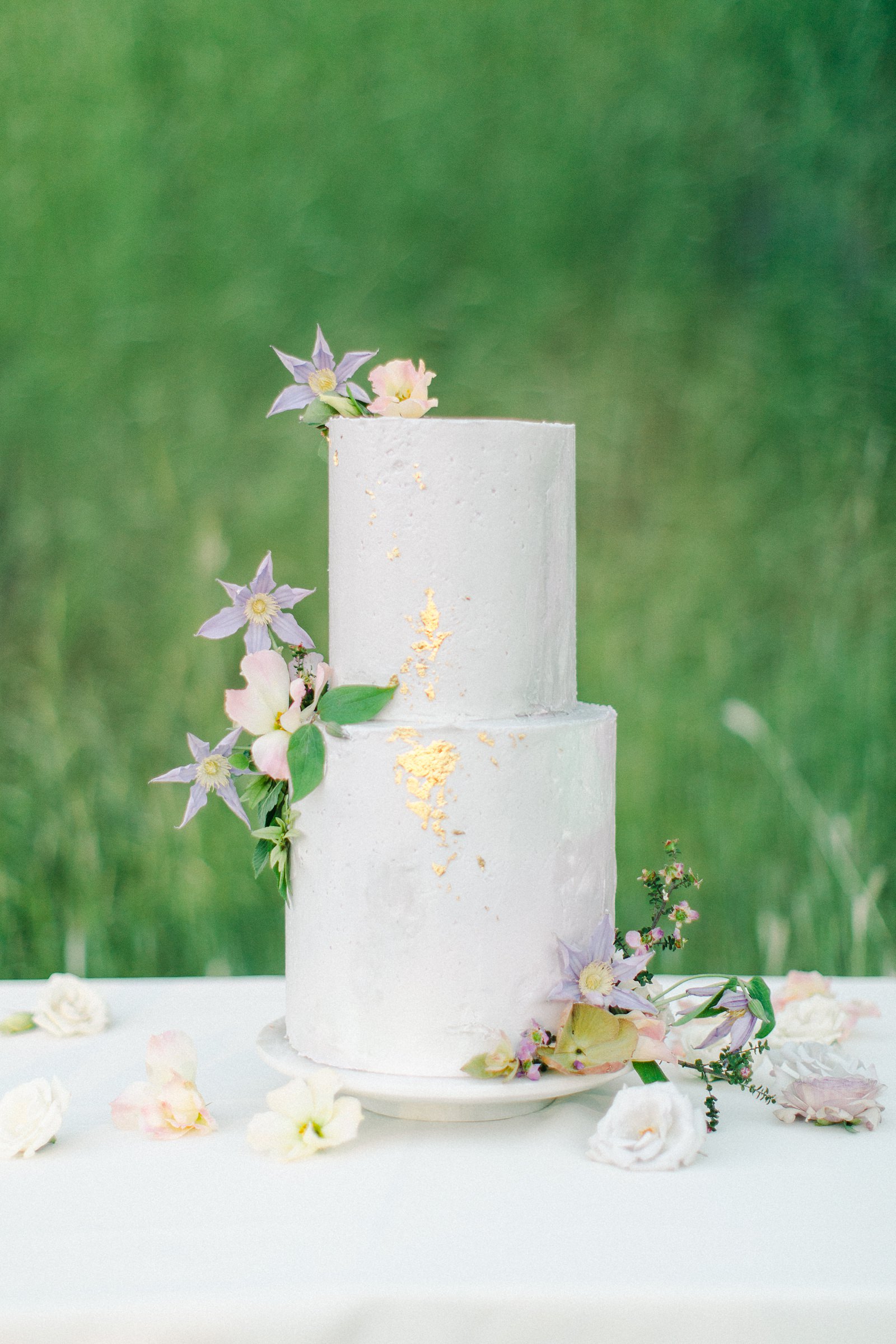 French pastel wedding , white and lavender two tier buttercream wedding cake with edible gold leaf and purple flowers, fine art film wedding photography