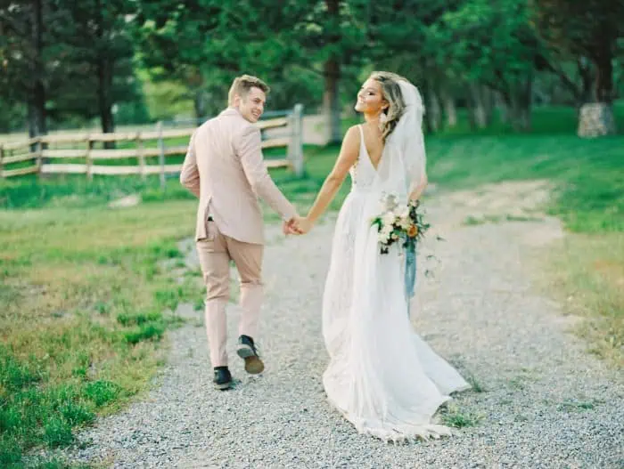 Wedding couple walking hand in hand outdoors, lush green background, romantic moment, Branson Maxwel.