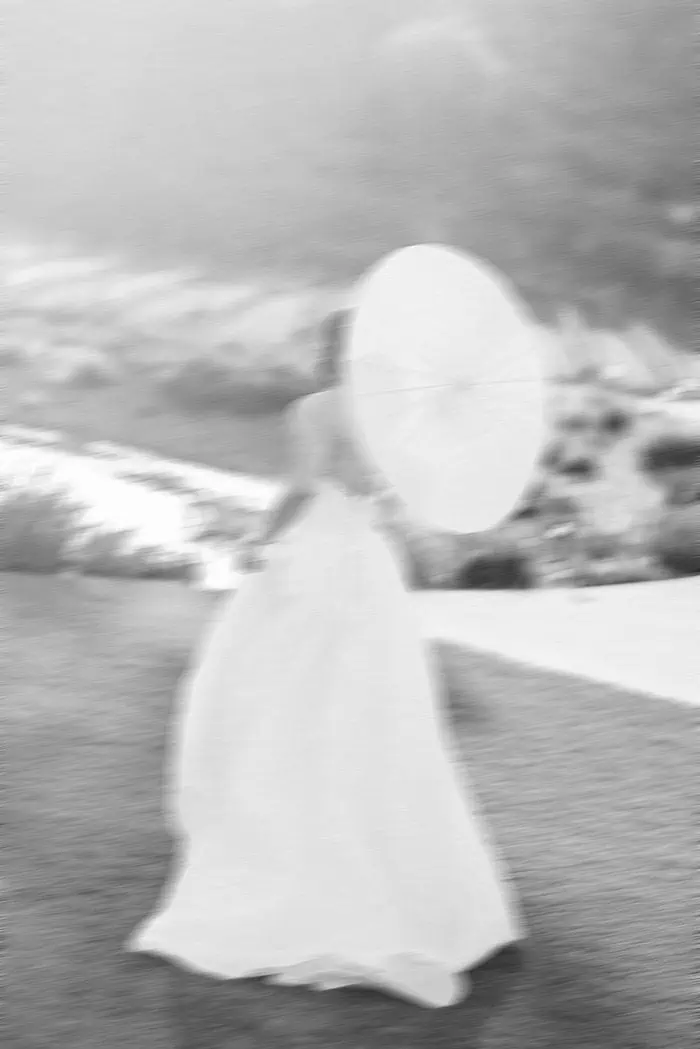 Woman walking with umbrella along shoreline at sunset.