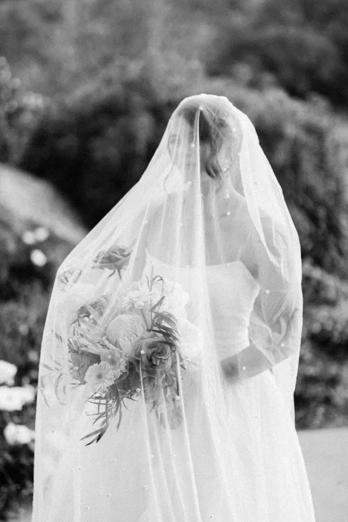Bride with veil holding bouquet in outdoor wedding scene.