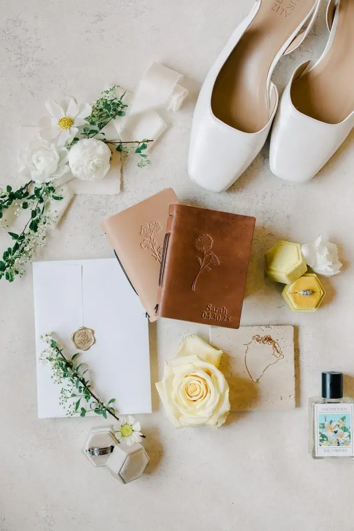 Elegant wedding flat lay with white shoes, floral accents, and personalized accessories.