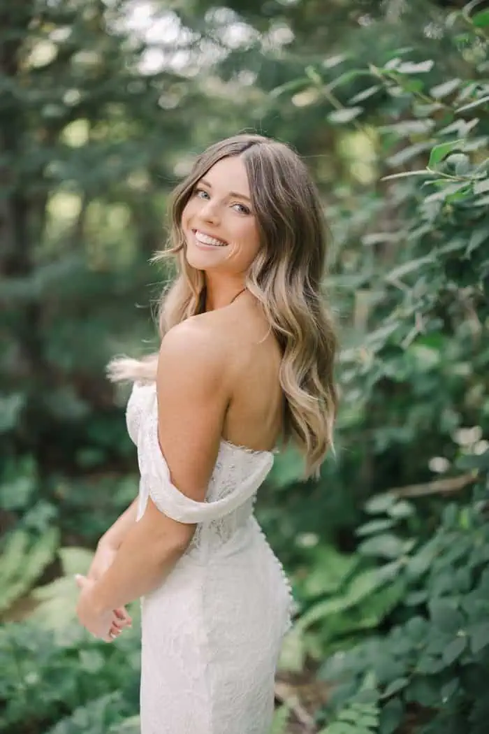 Elegant woman in a white dress smiling in a lush green garden setting.