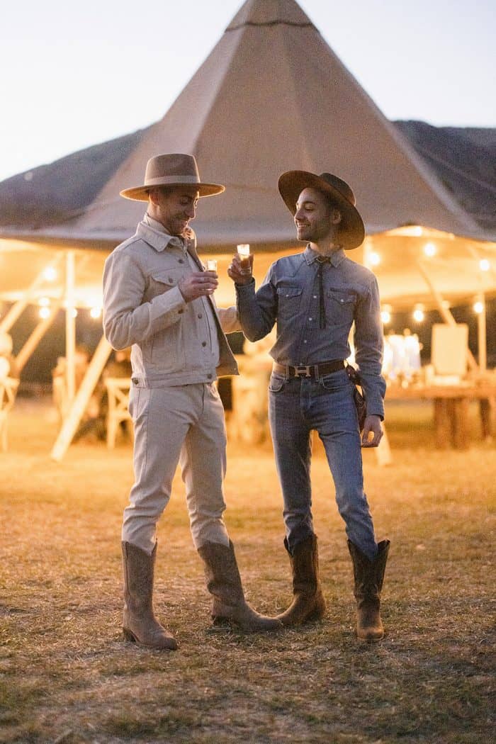 Two men in cowboy hats enjoying drinks at a Western-themed event.