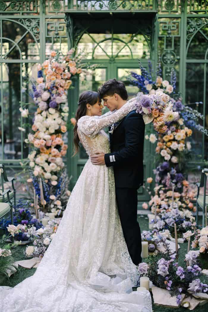 Elegant wedding couple embracing in a lush floral garden backdrop.