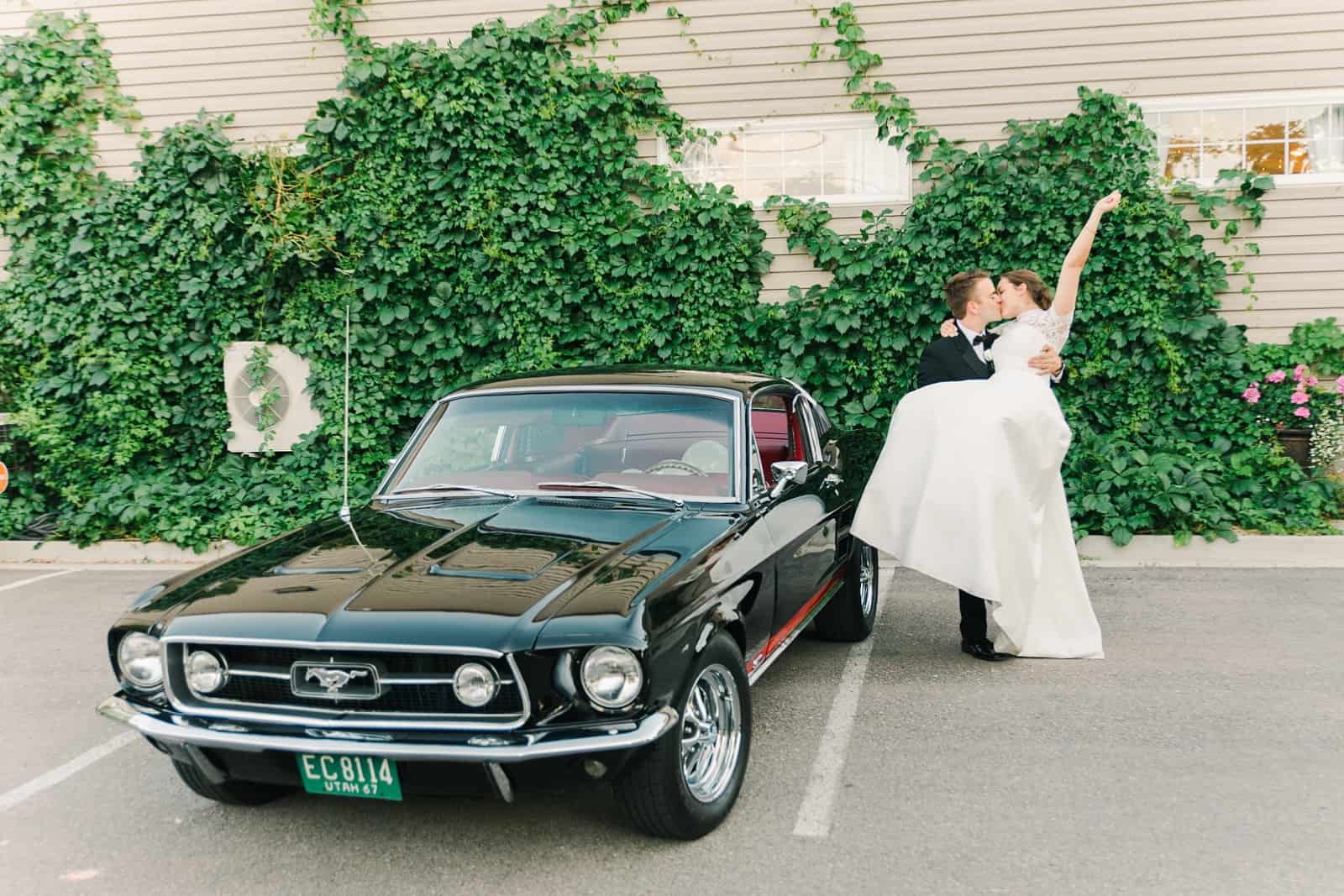 Clarion Gardens Payson Utah Wedding, bride and groom pose with black vintage Mustang convertible reception getaway car