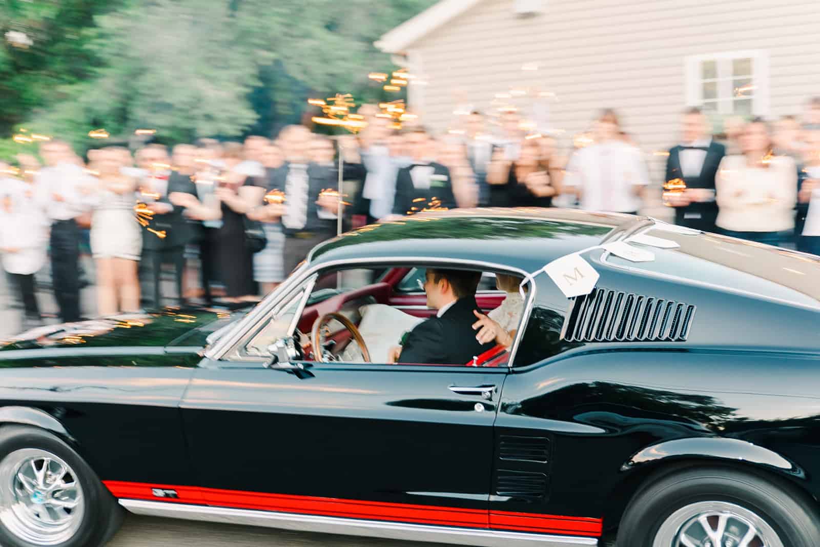 Clarion Gardens Payson Utah Wedding, bride and groom drive away in black vintage Mustang convertible reception getaway car