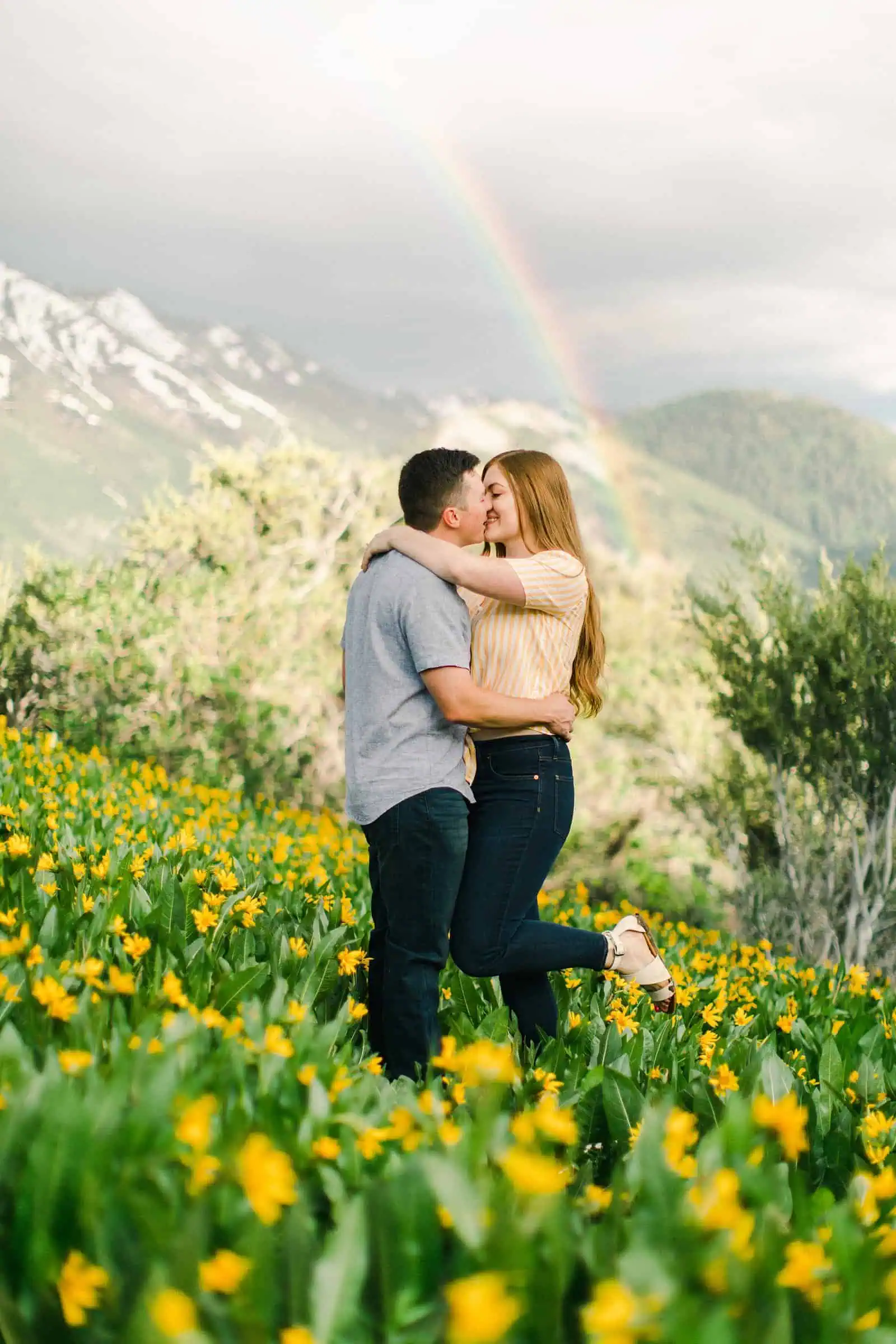 Provo Canyon wildflowers field engagement session, Utah wedding photography, engaged couple kissing in yellow flowers and mountains with rainbow in background