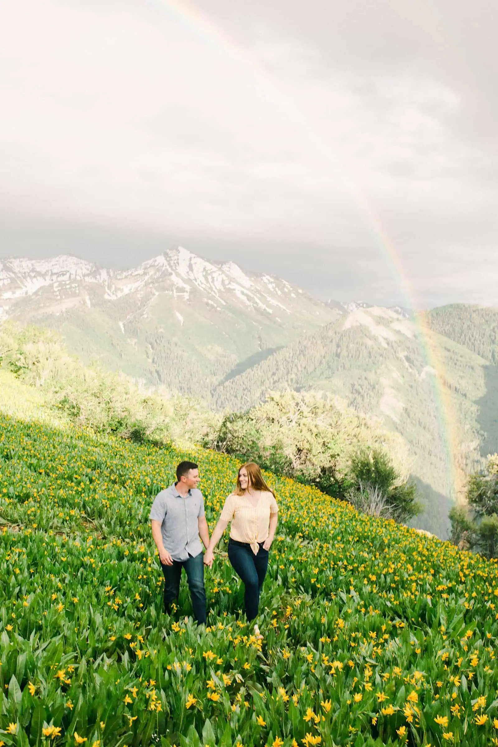 Provo Canyon wildflowers field engagement session, Utah wedding photography, engaged couple walking in yellow flowers and mountains with rainbow in background