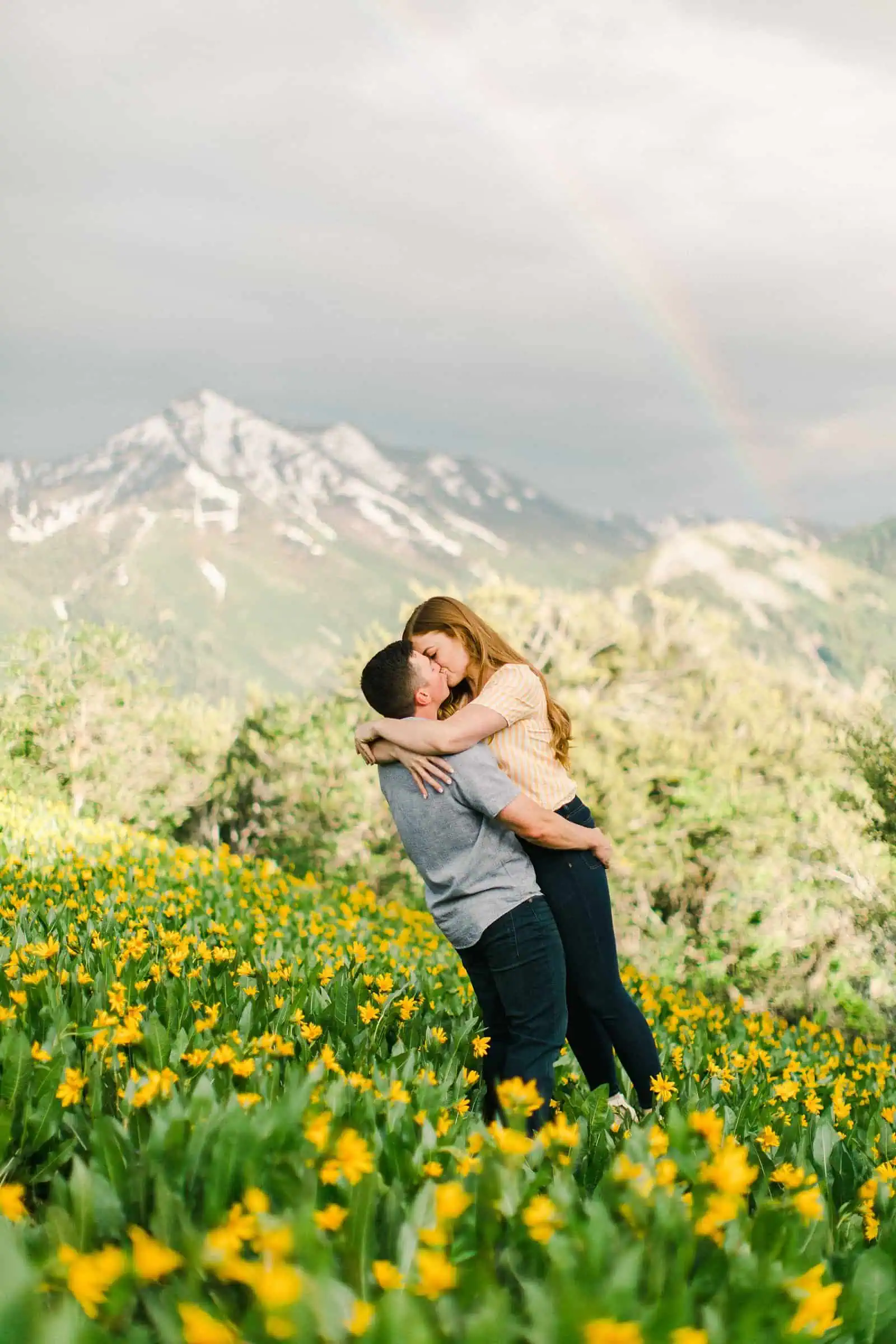 Provo Canyon wildflowers field engagement session, Utah wedding photography, engaged couple kissing in yellow flowers and mountains with rainbow in background