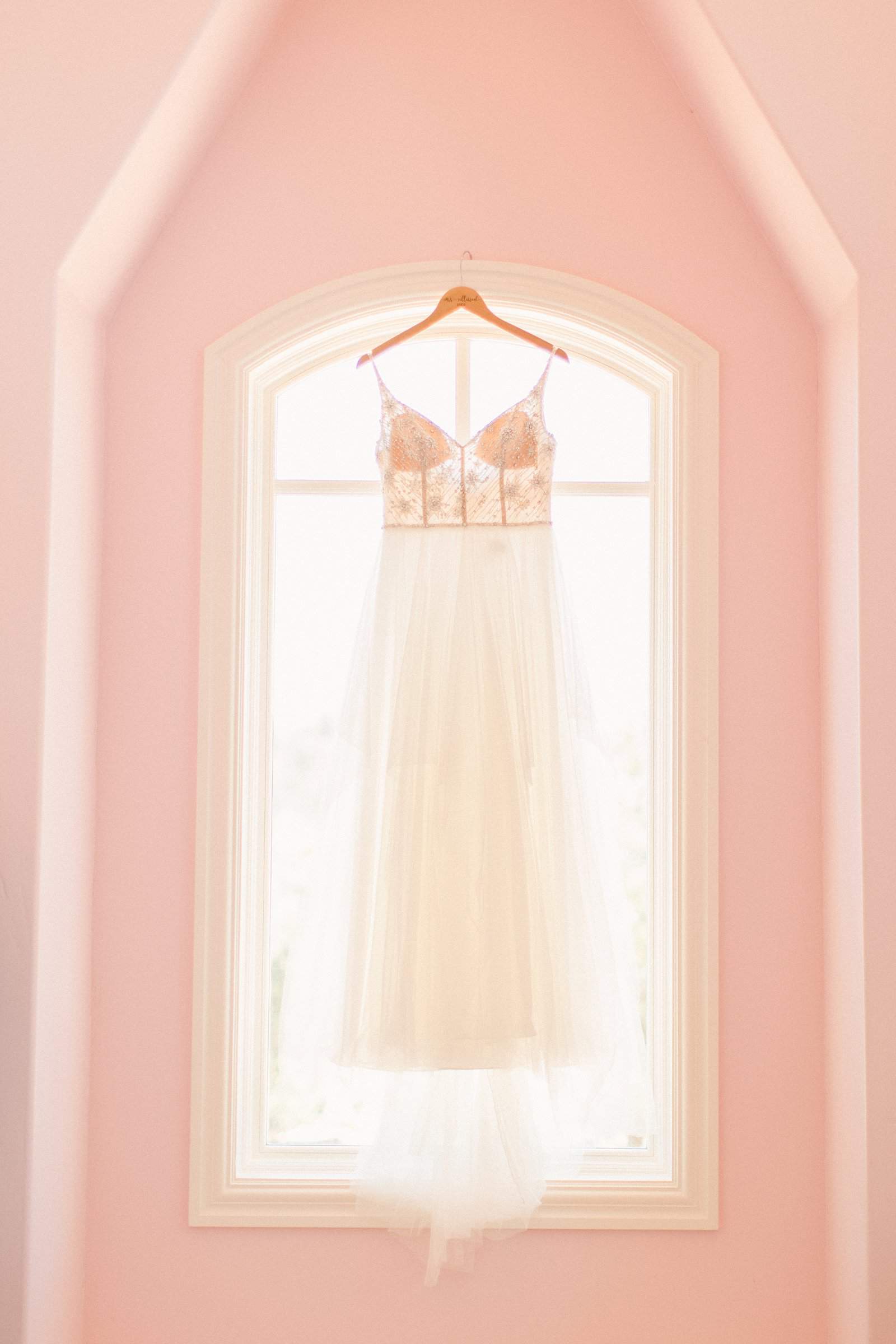 v neck wedding dress hangs in window with pink wall