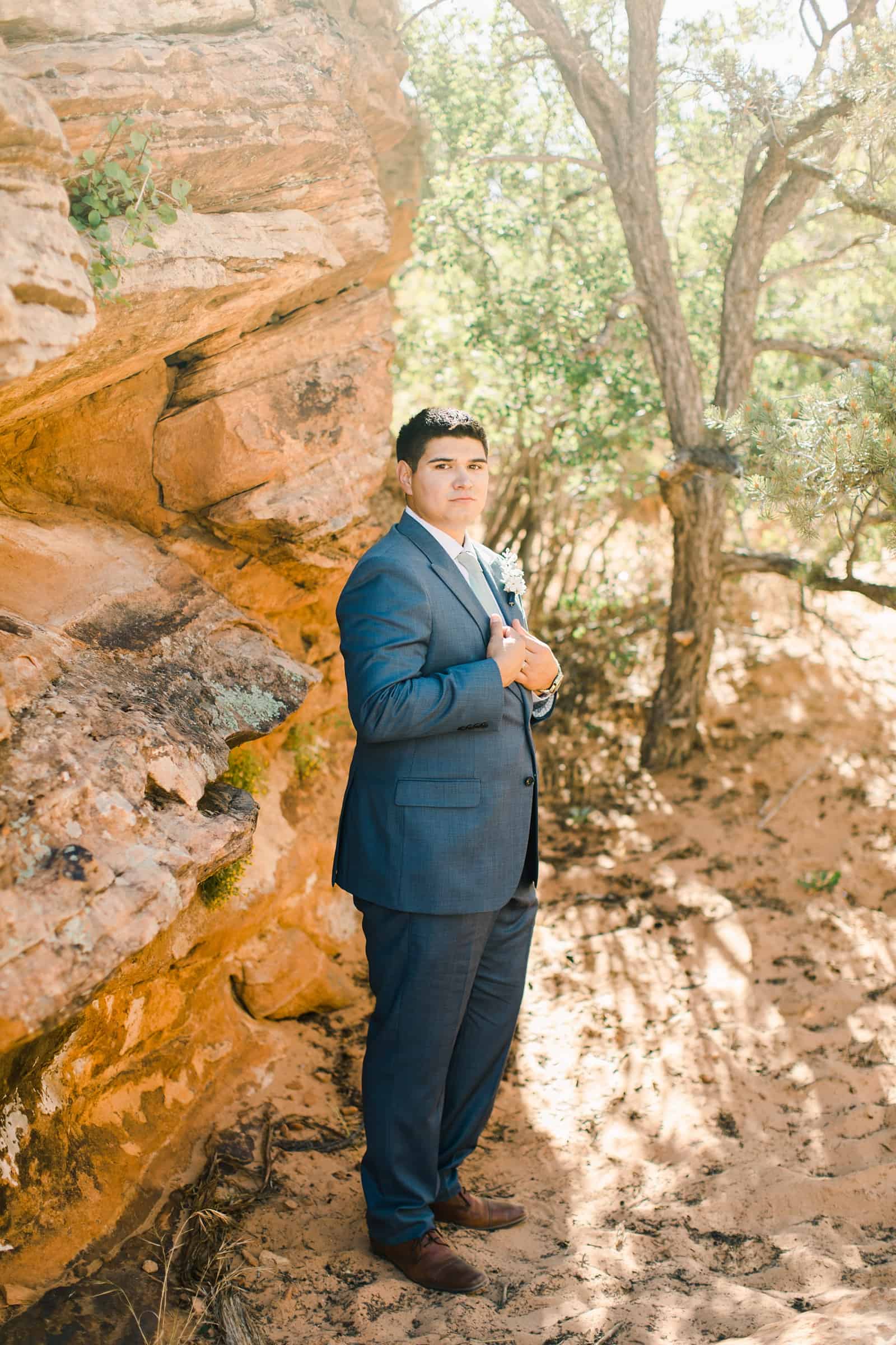 groom in gray suit poses near red rocks