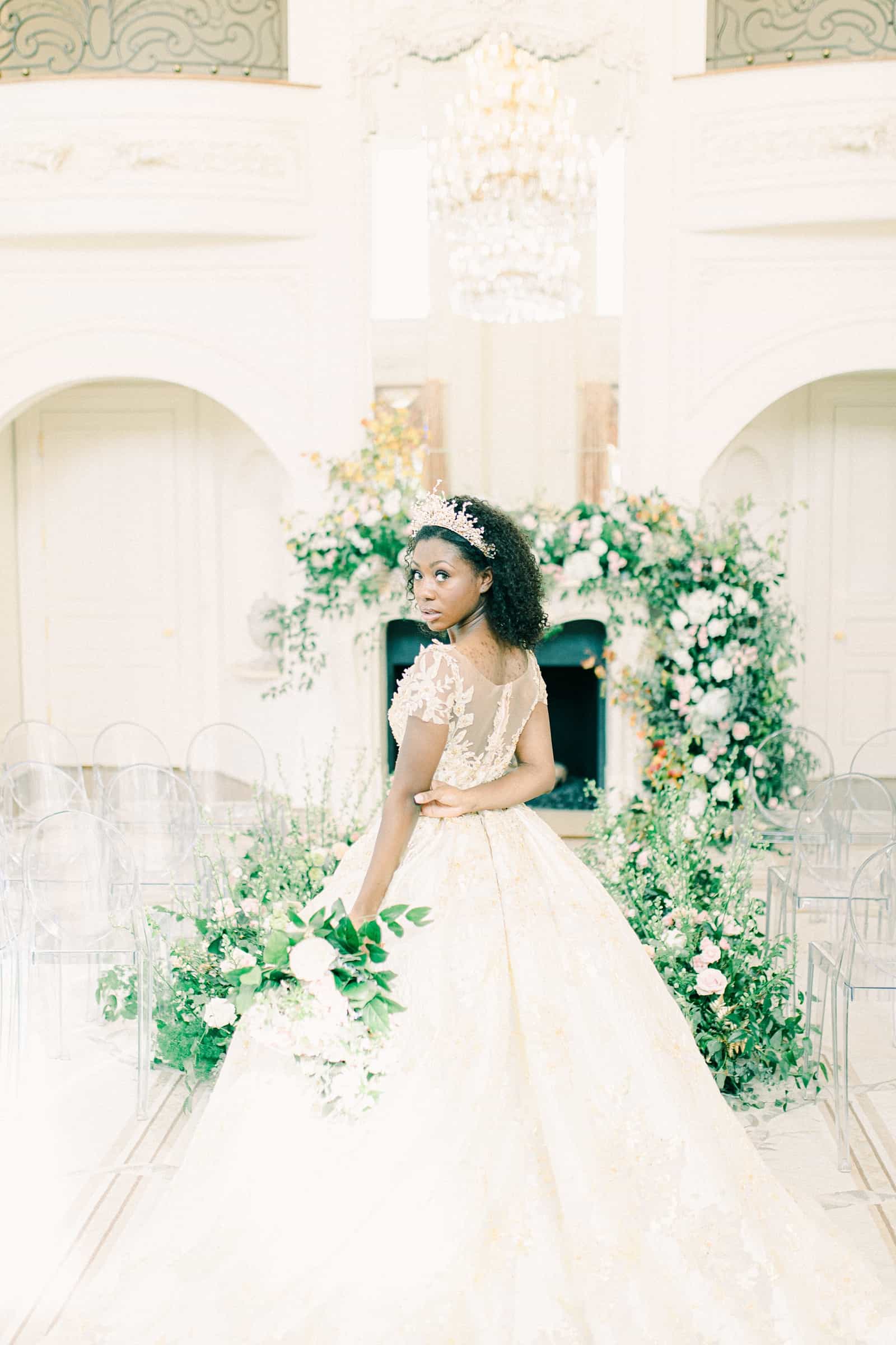 Disney princess bride with tiara in front of greenery and floral arch, garland ceremony decor