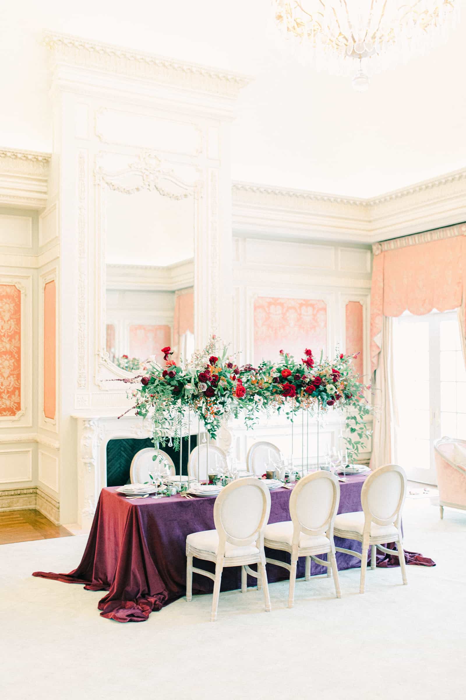 Wedding table with floral arch, maroon tablecloth in European style mansion