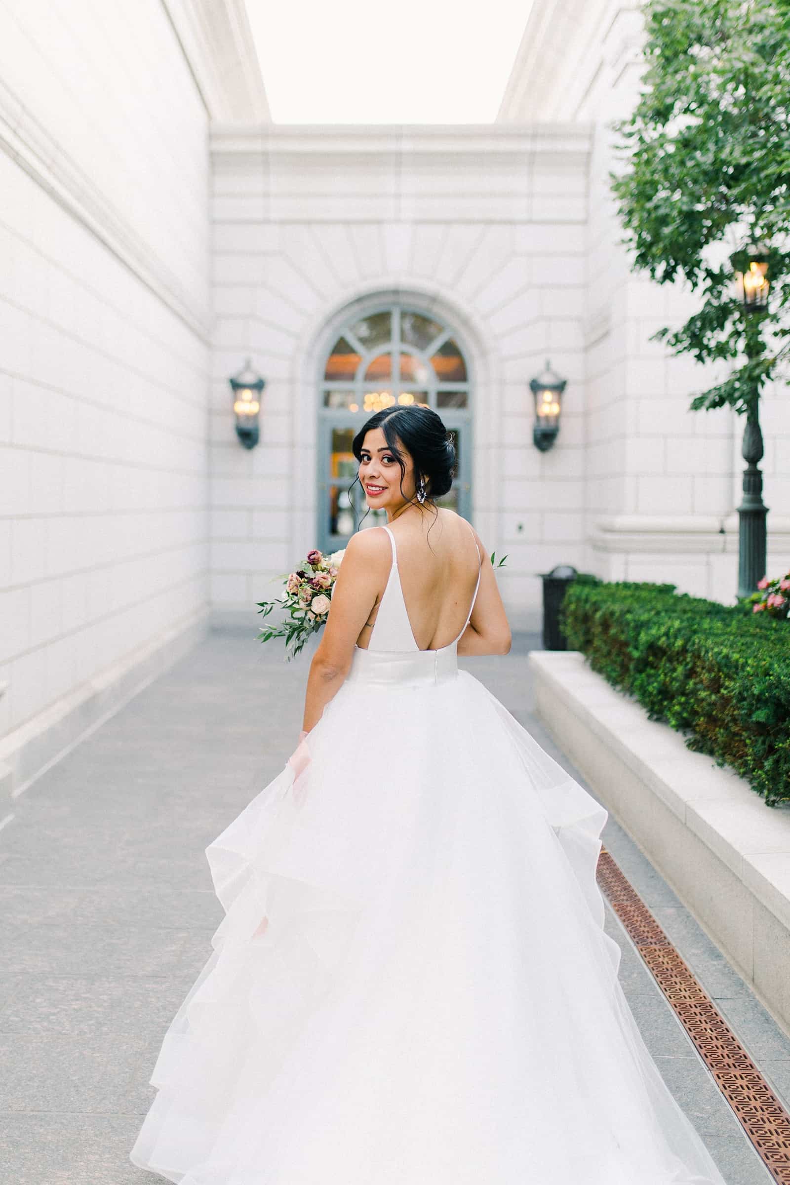 Bride with long train and low back dress in the courtyard of the Grand America Hotel in Salt Lake City, Utah