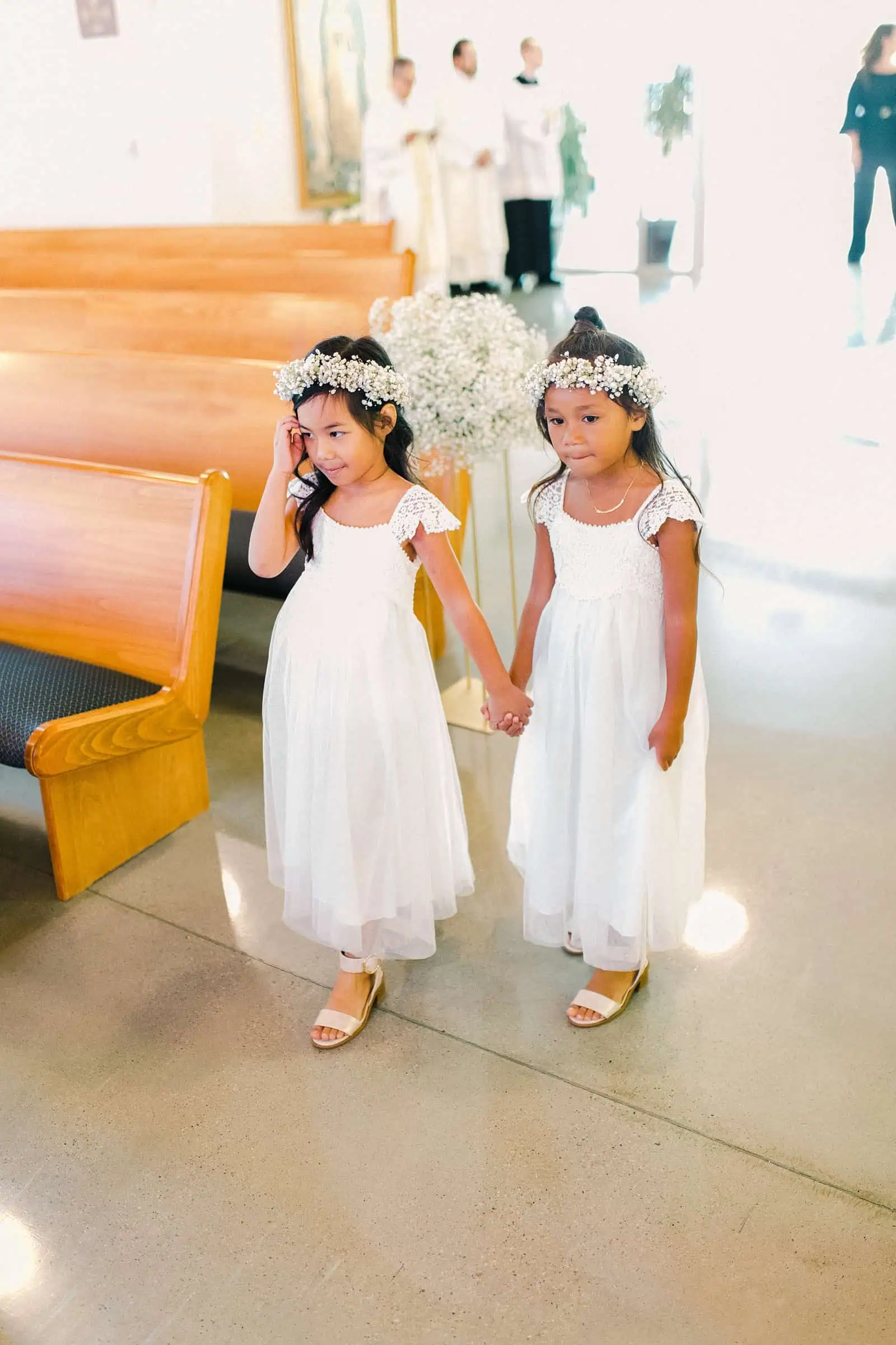 Flower girls with baby's breath flower crowns and white dresses walk down the aisle