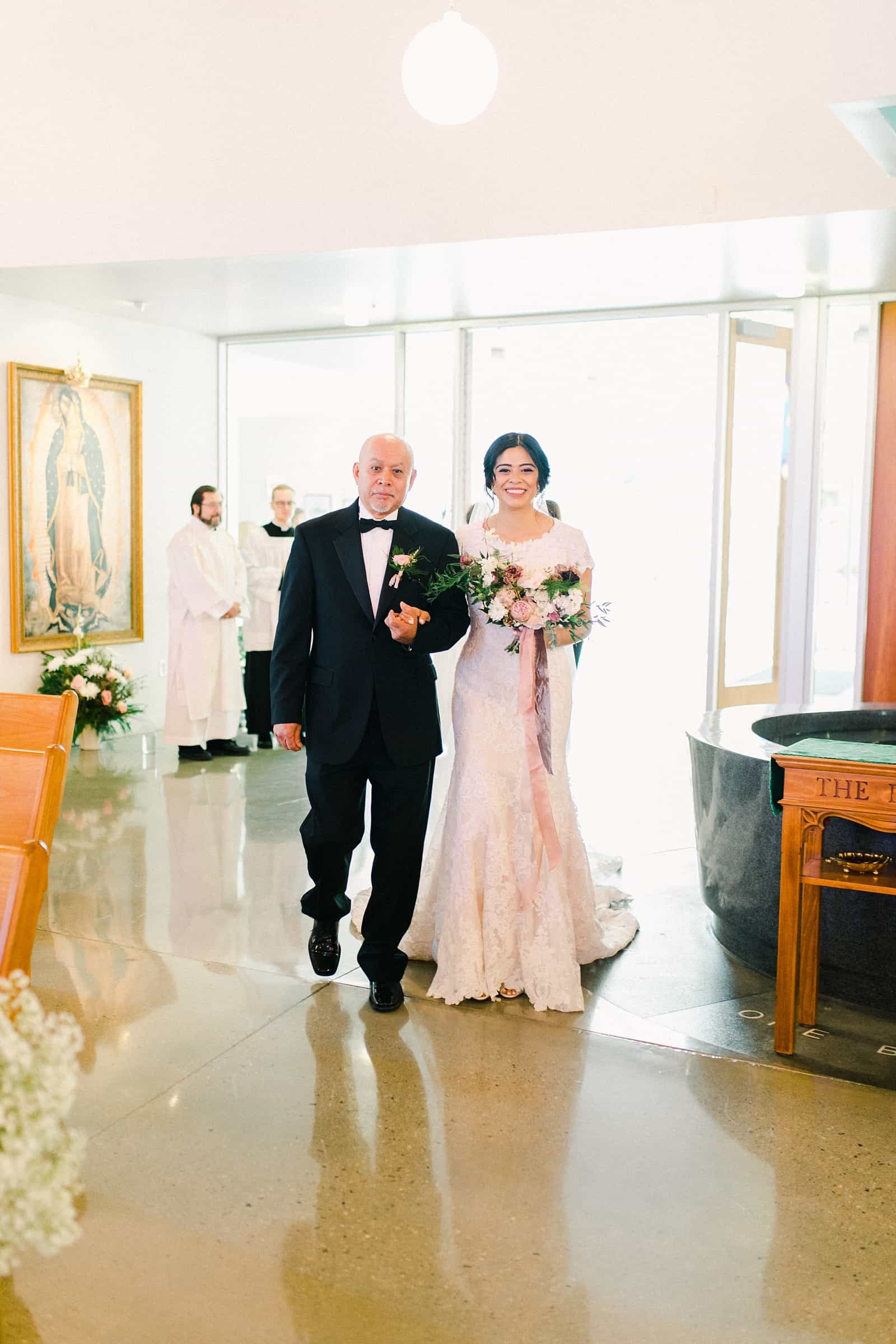 father of the bride walks her down the aisle in traditional Catholic ceremony