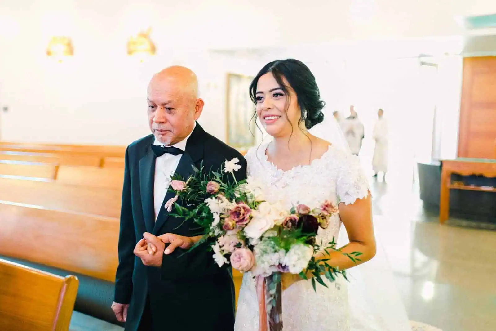 father of the bride walks her down the aisle in traditional Catholic cathedral ceremony