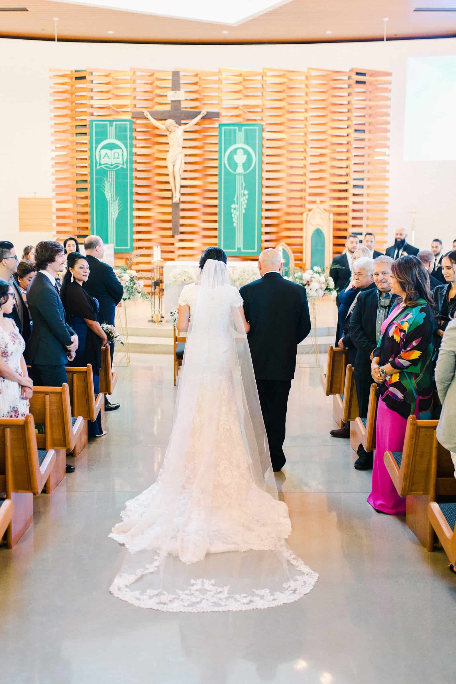 father of the bride walks her down the aisle in traditional Catholic ceremony