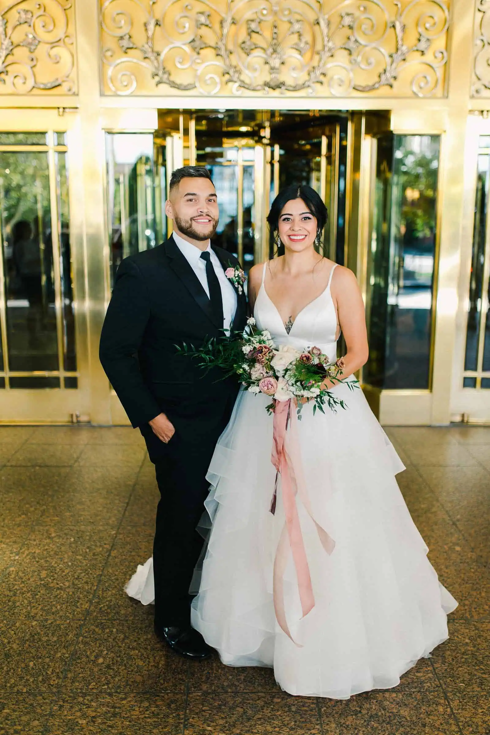 Bride and groom smile in front of gold doors