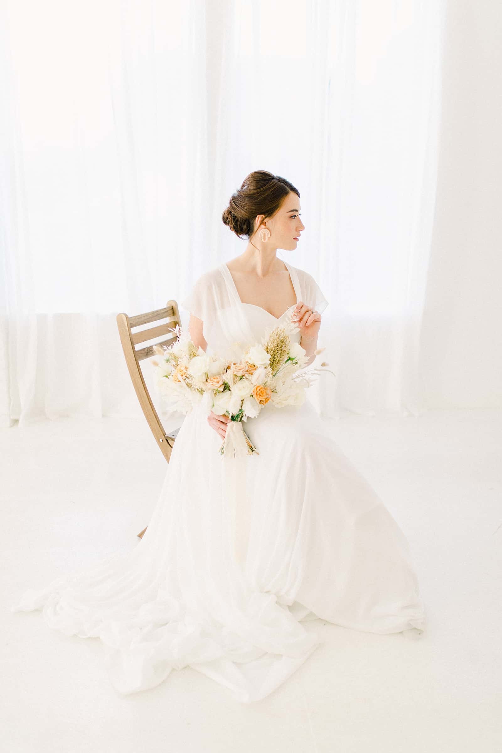 Modern bride sitting with simple, neutral bouquet and sweetheart neckline