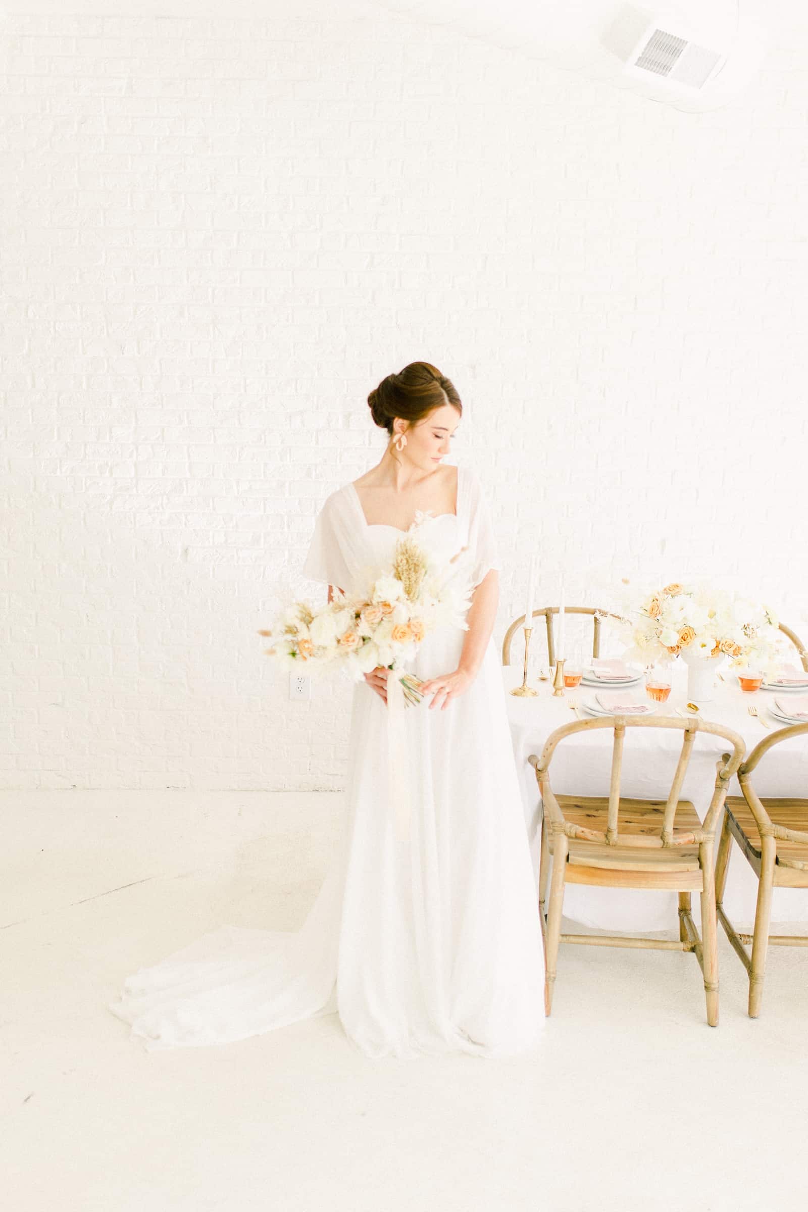 Bride standing next to Modern wedding table settings with white tablecloth and neutral colors