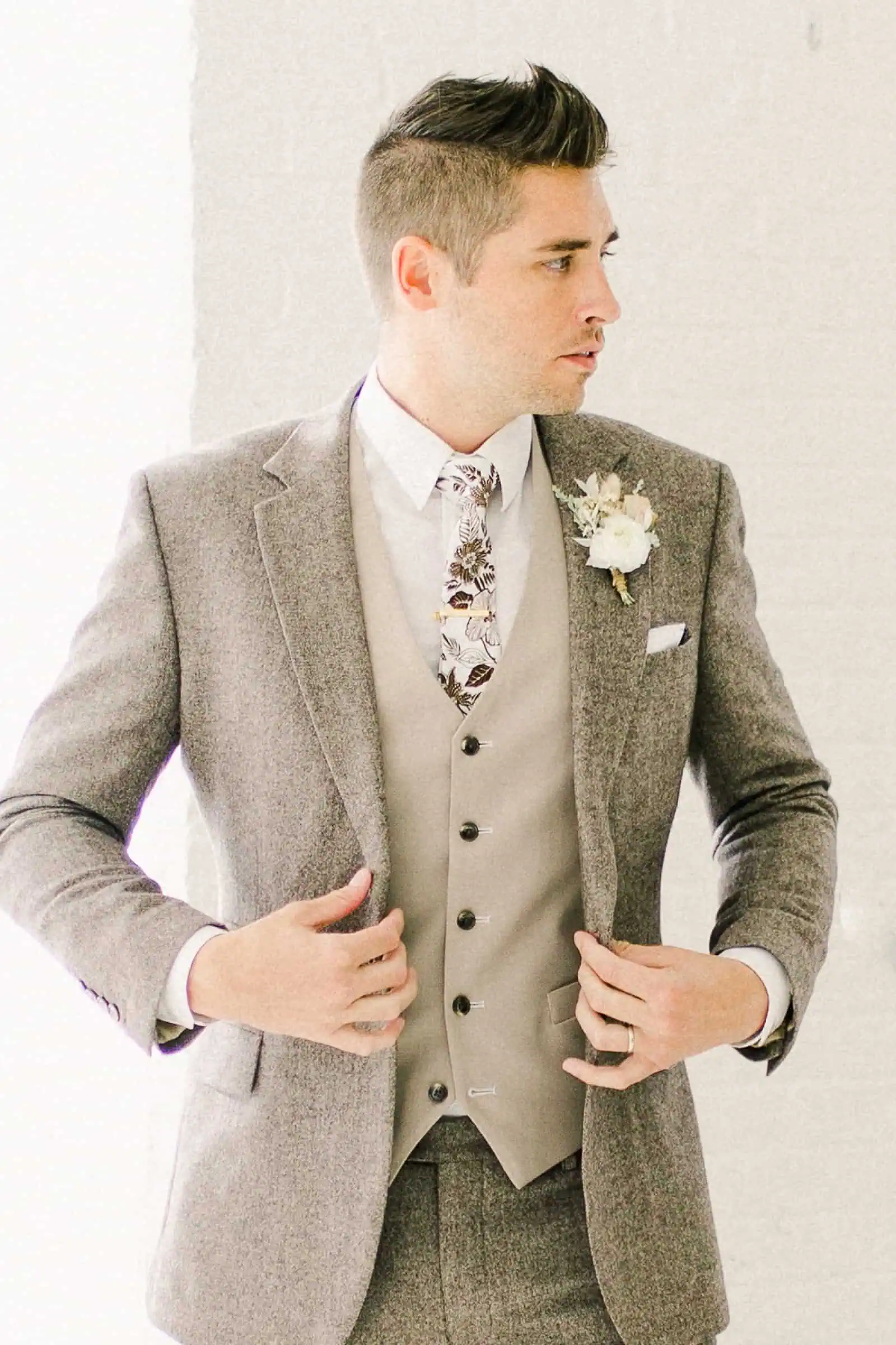 Modern groom wearing oatmeal gray custom three piece suit with fall floral tie and a vest