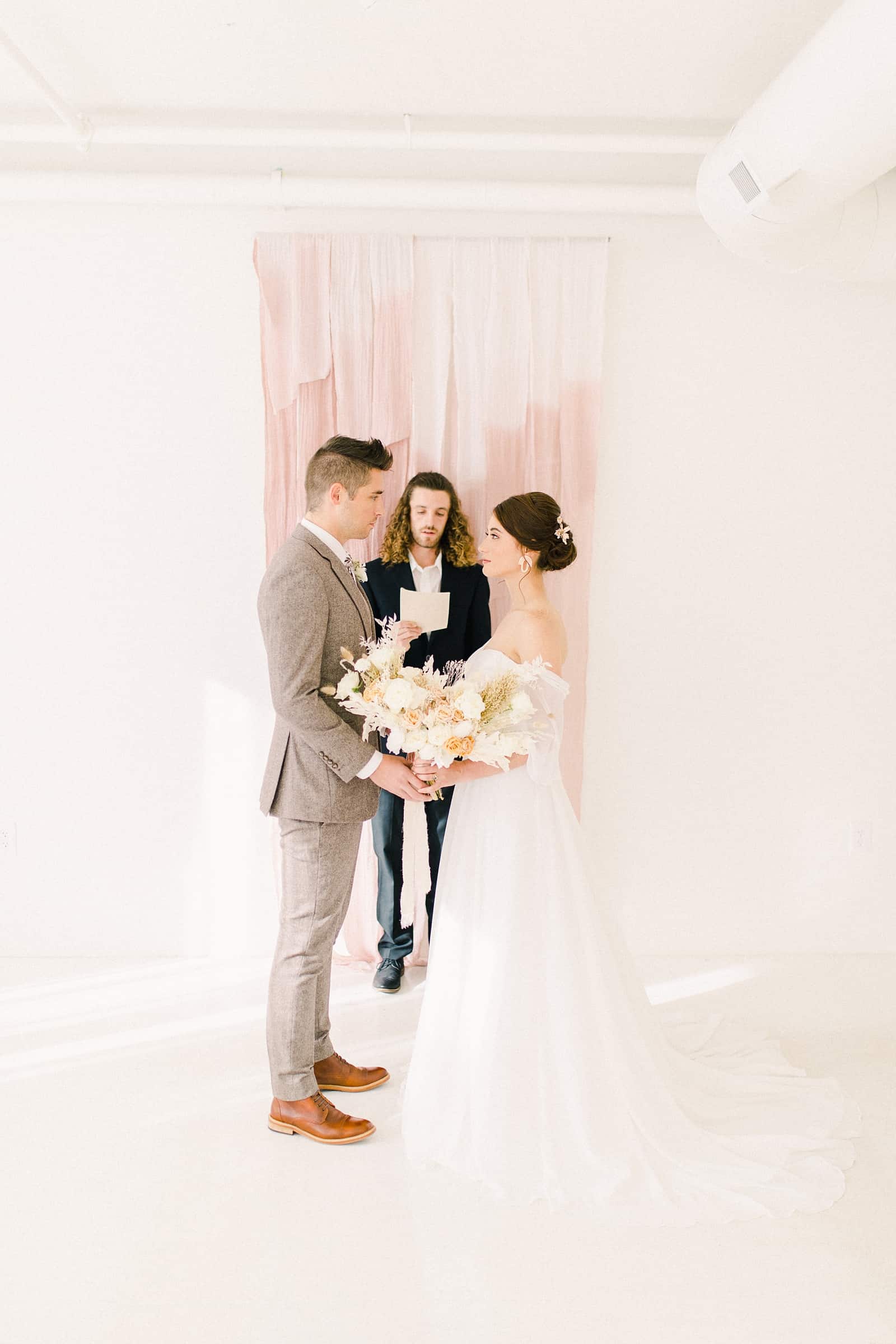 Wedding ceremony with friend of the bride and groom officiant in front of blush pink ombre watercolor backdrop