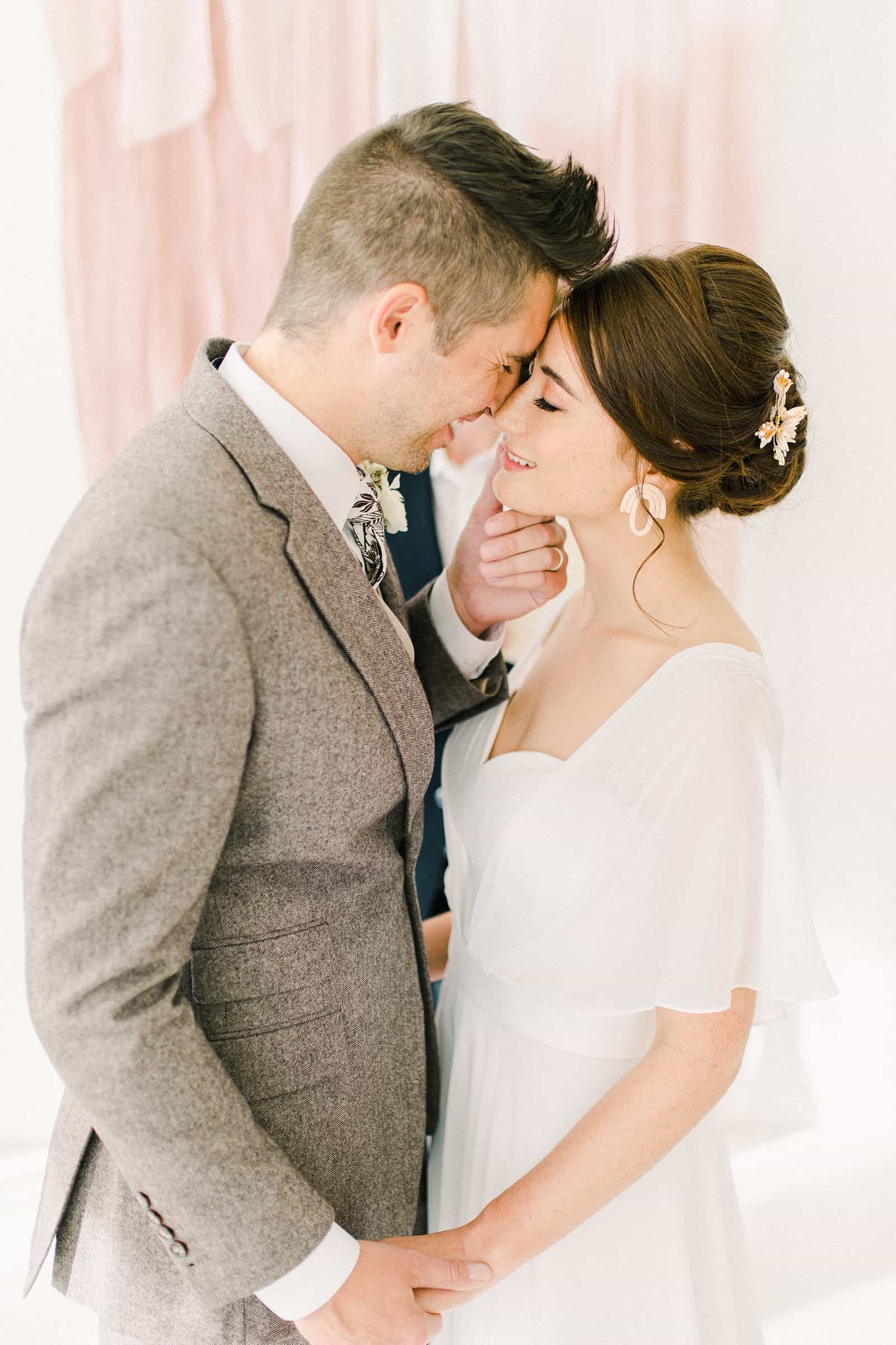 Bride and groom first kiss in front of blush pink painted ombre watercolor backdrop