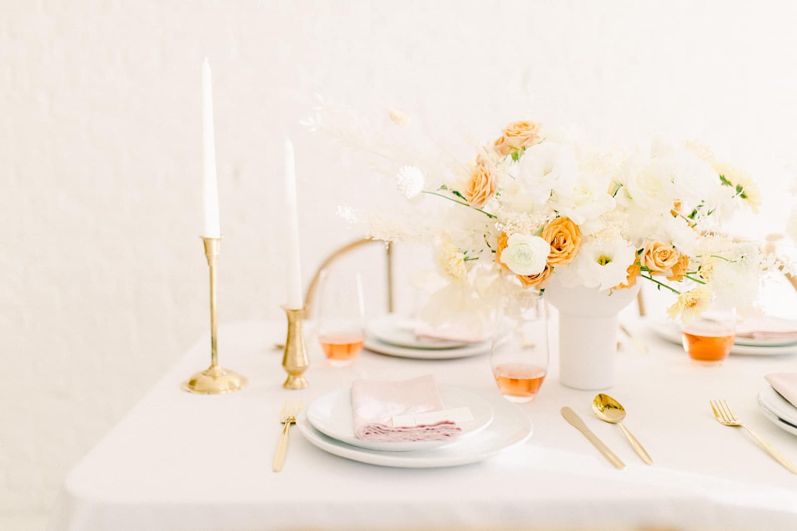 Modern wedding table scape with white and orange flower centerpiece and blush pink napkins and gold candlesticks