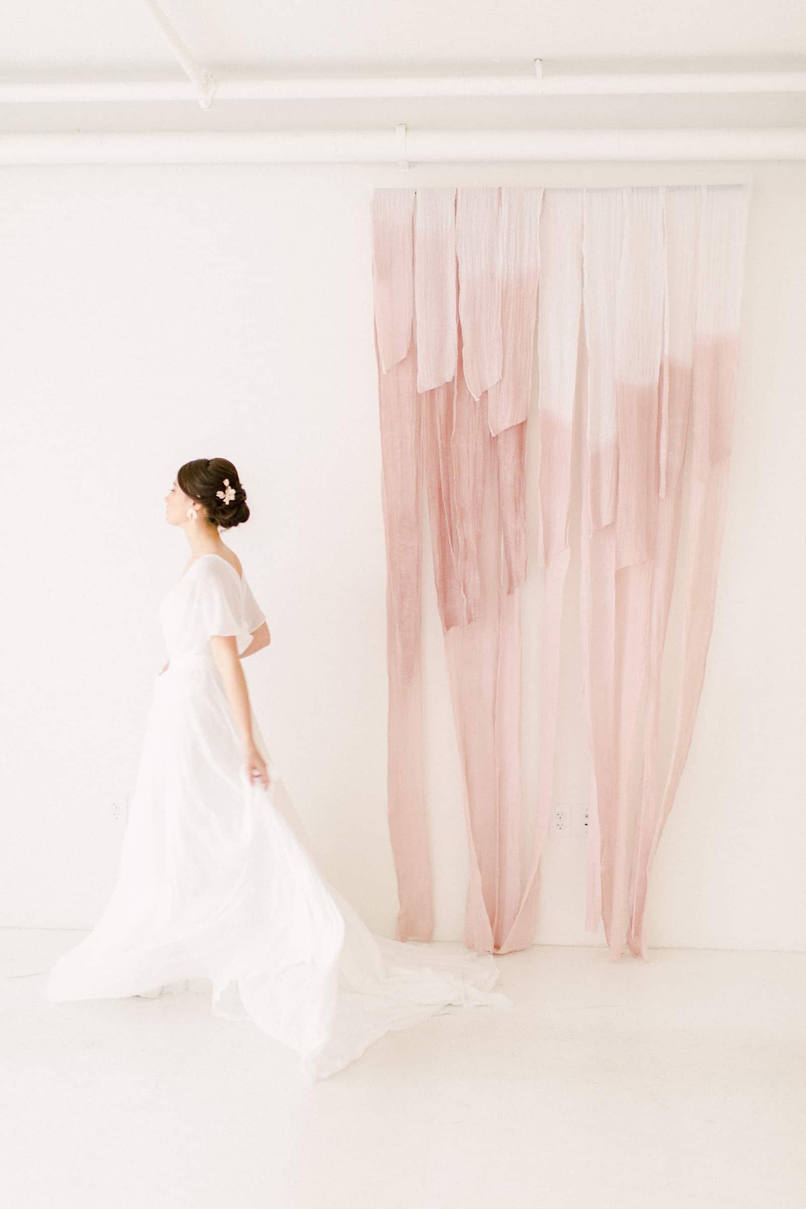 Modern bride walks in front of blush pink painted cheesecloth ombre watercolor backdrop