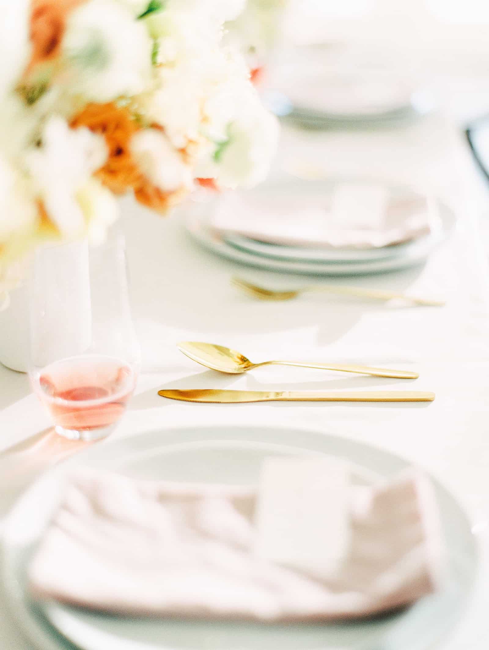 Modern wedding table scape with white and orange flower centerpiece and blush pink napkins and gold cutlery