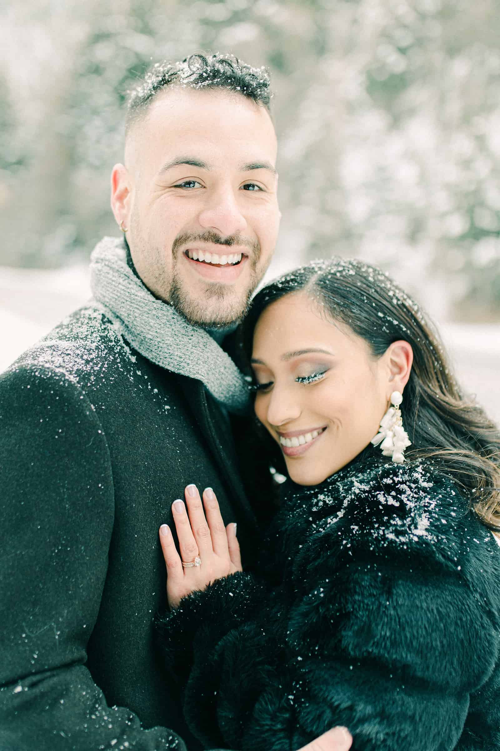 Smiling in the snow, gray scarf and black faux fur coat, engagement ring