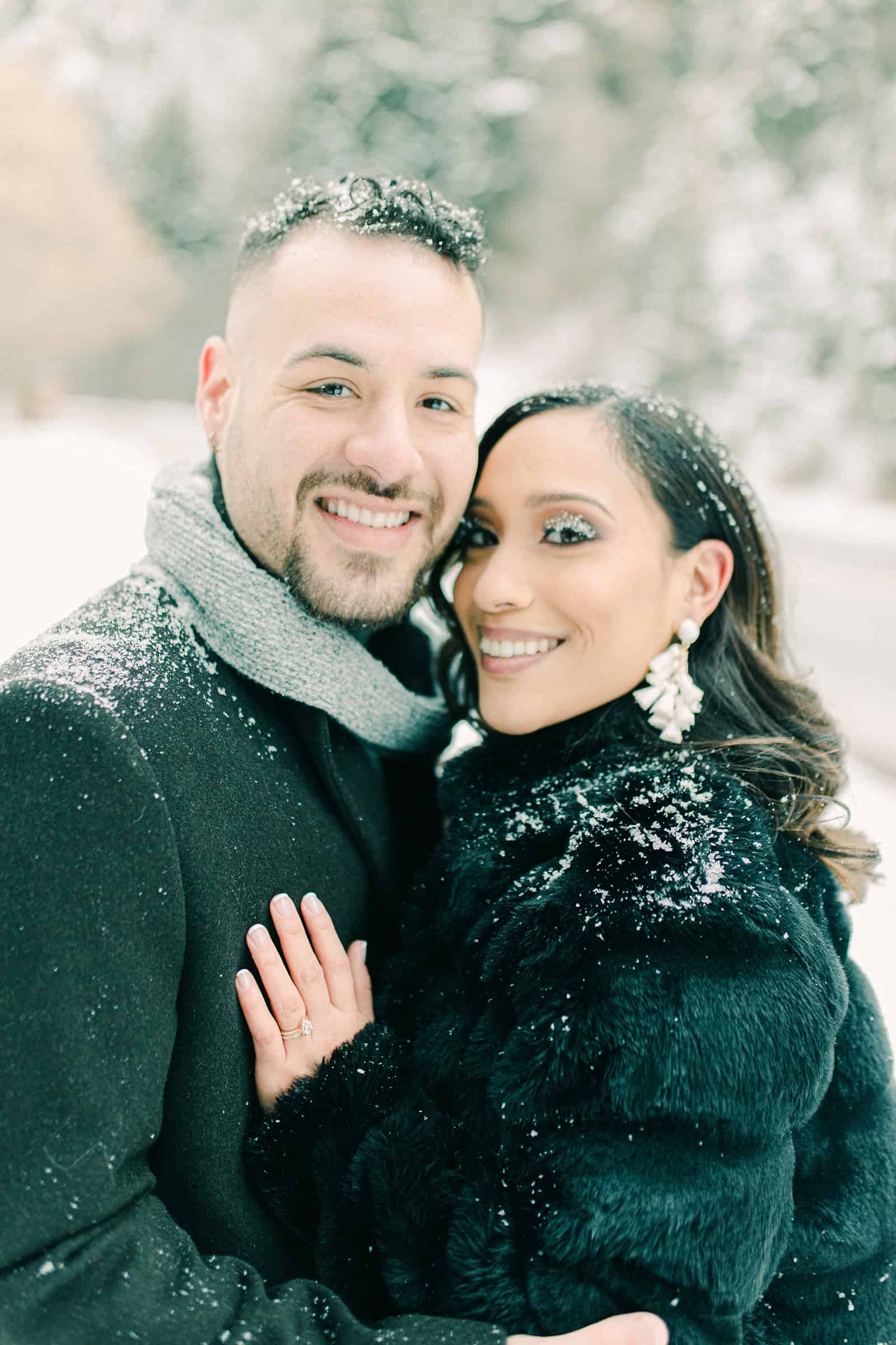 Couple smiling in snowy winter engagement session, snow on eyelashes