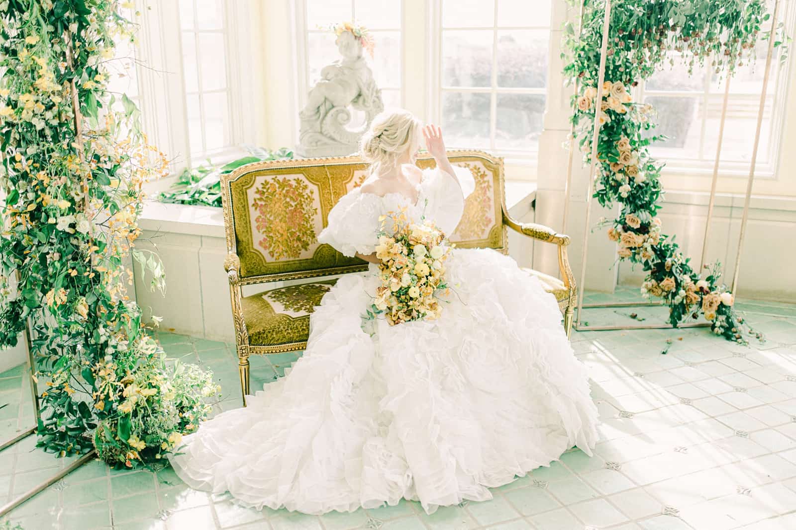 Bride in ball gown sitting on French inspired bench on wedding day