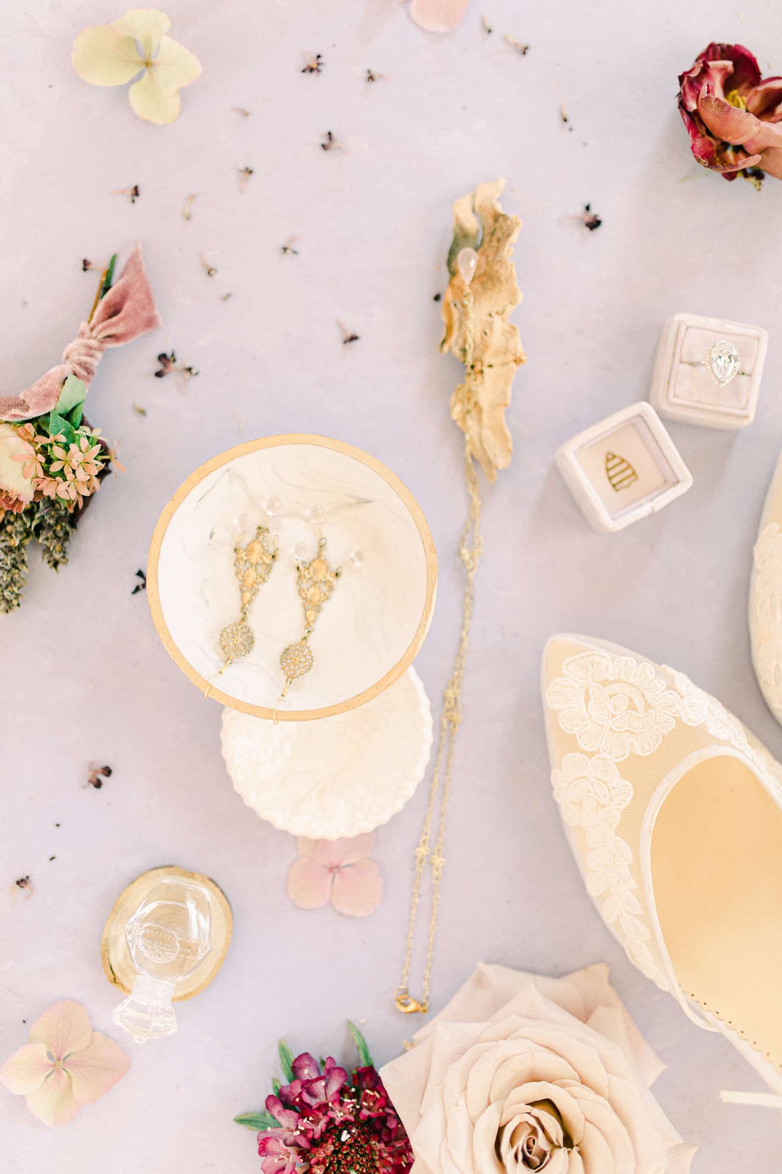 Fine art wedding details flat lay with purple tablecloth and designer shoes for the bride, gold wedding earrings