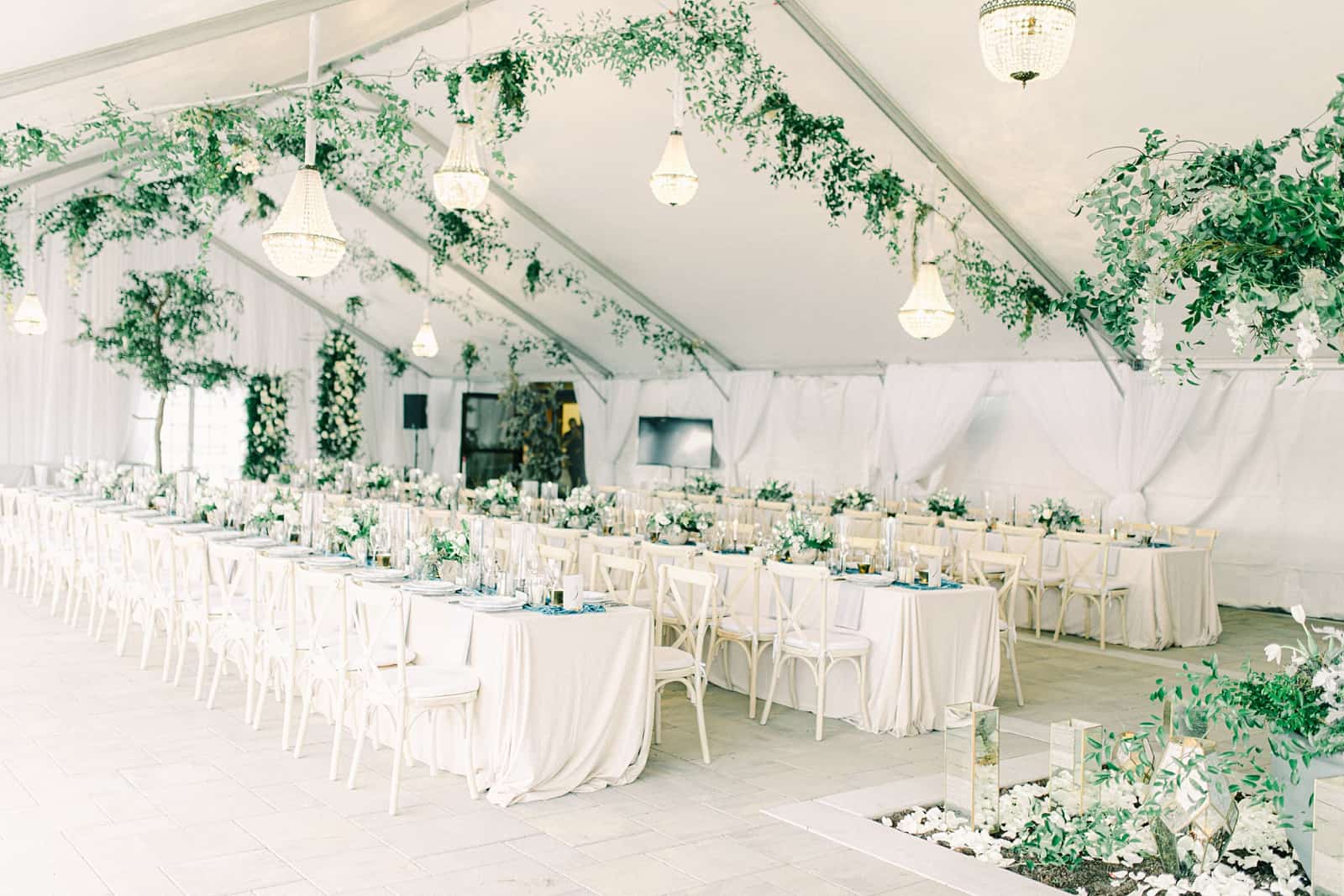 Luxury winter wedding inside white tent reception with greenery floral garland with white roses and tables with centerpieces