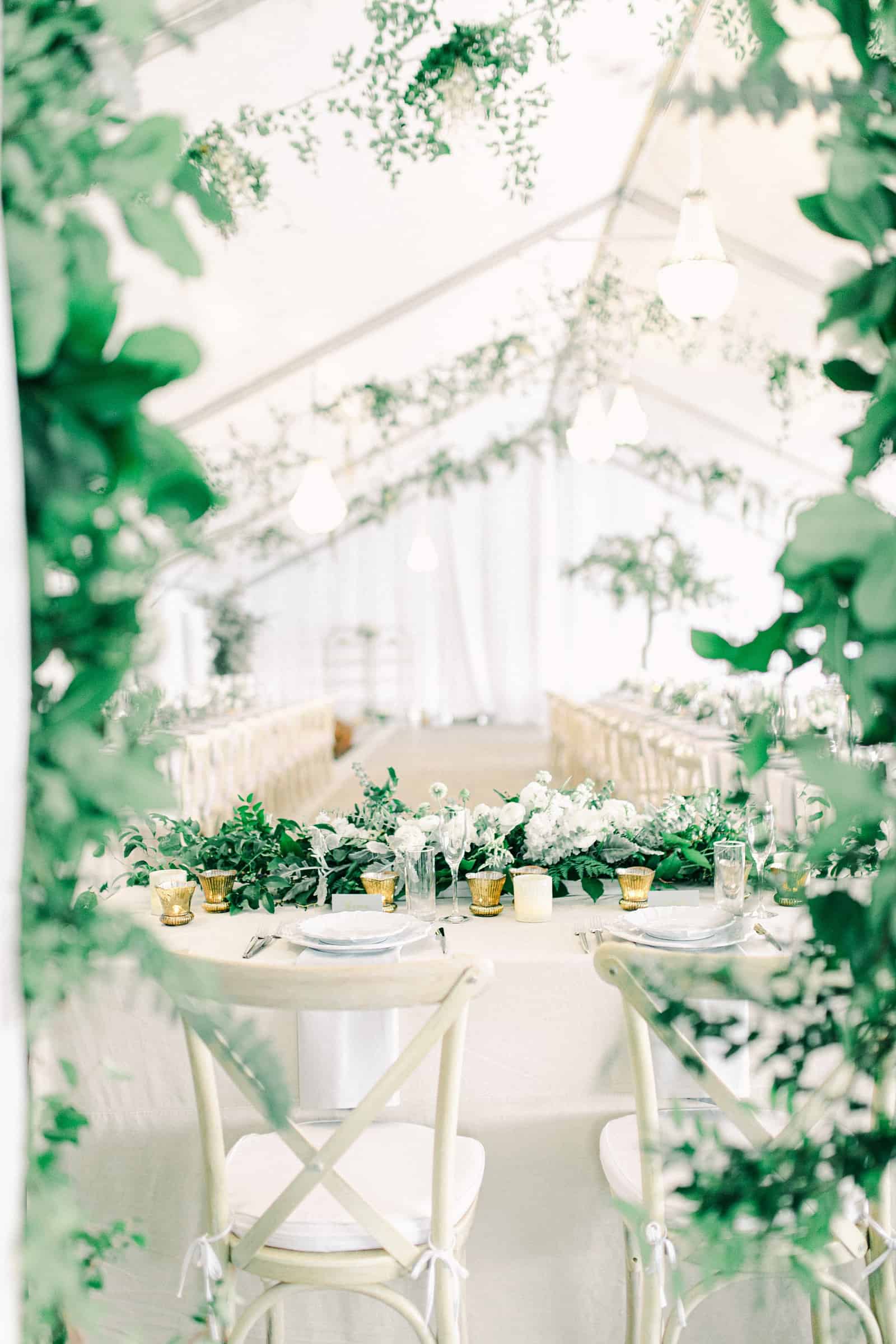 Luxury winter wedding inside white tent reception with greenery floral garland with white roses and tables with centerpieces