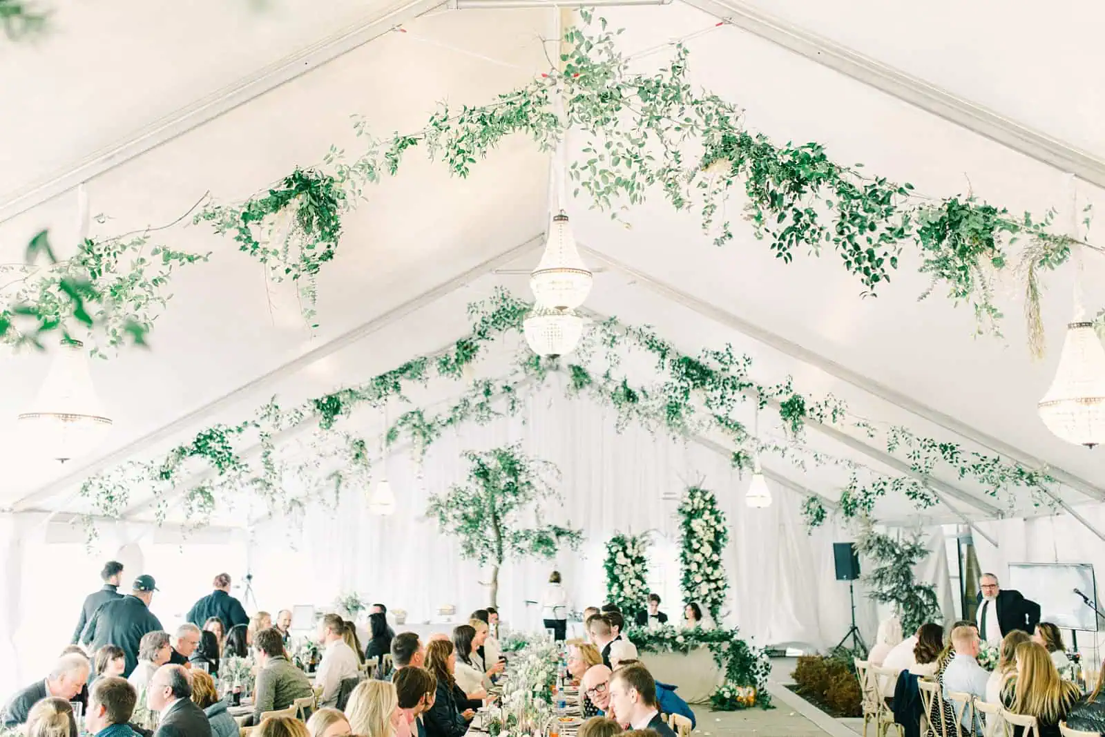 Luxury winter wedding inside white tent reception with greenery floral garland with white roses and tables with centerpieces