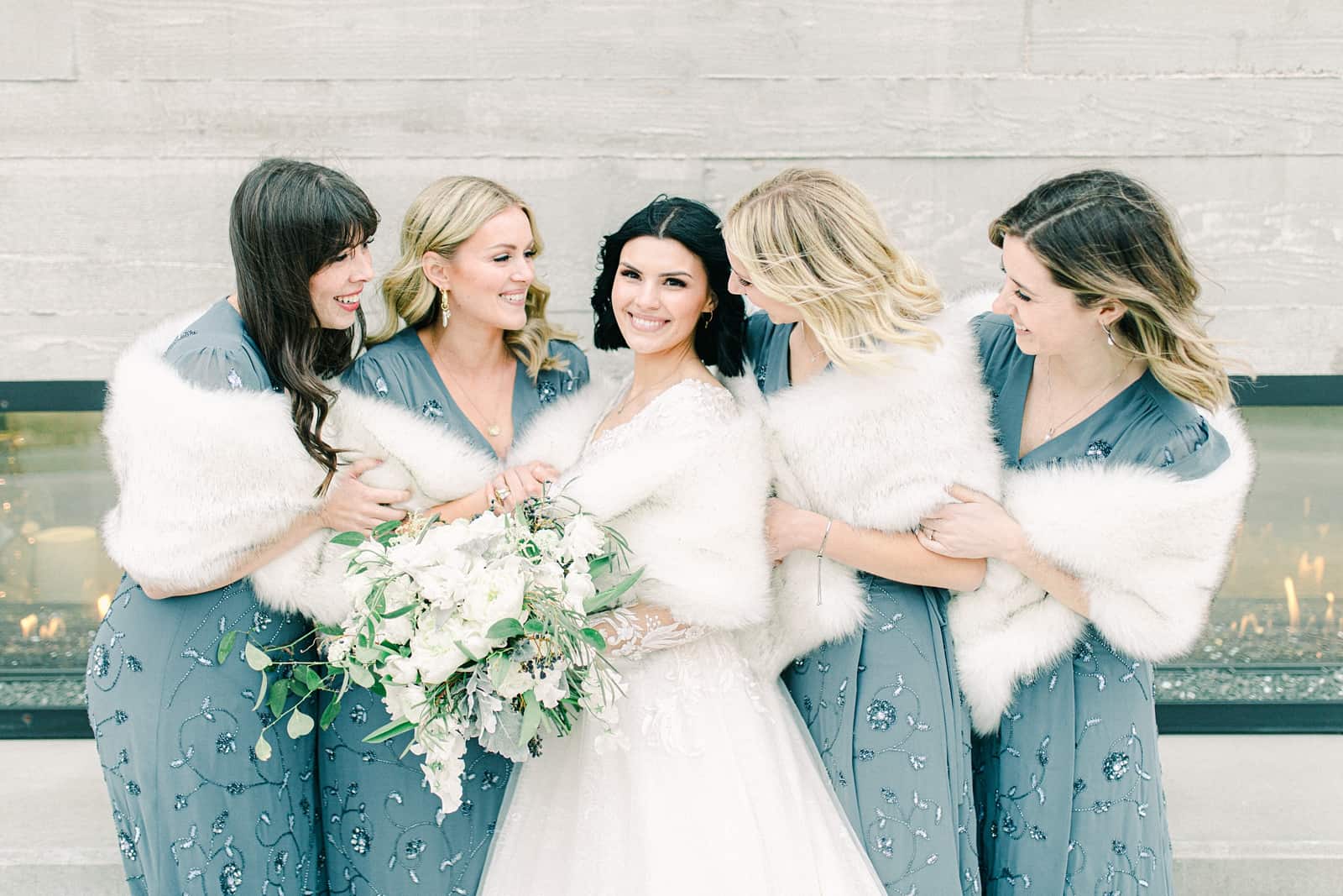 Winter wedding bride with bridesmaids, blue beaded bridesmaids dresses with white fur stoles, white flower bouquets