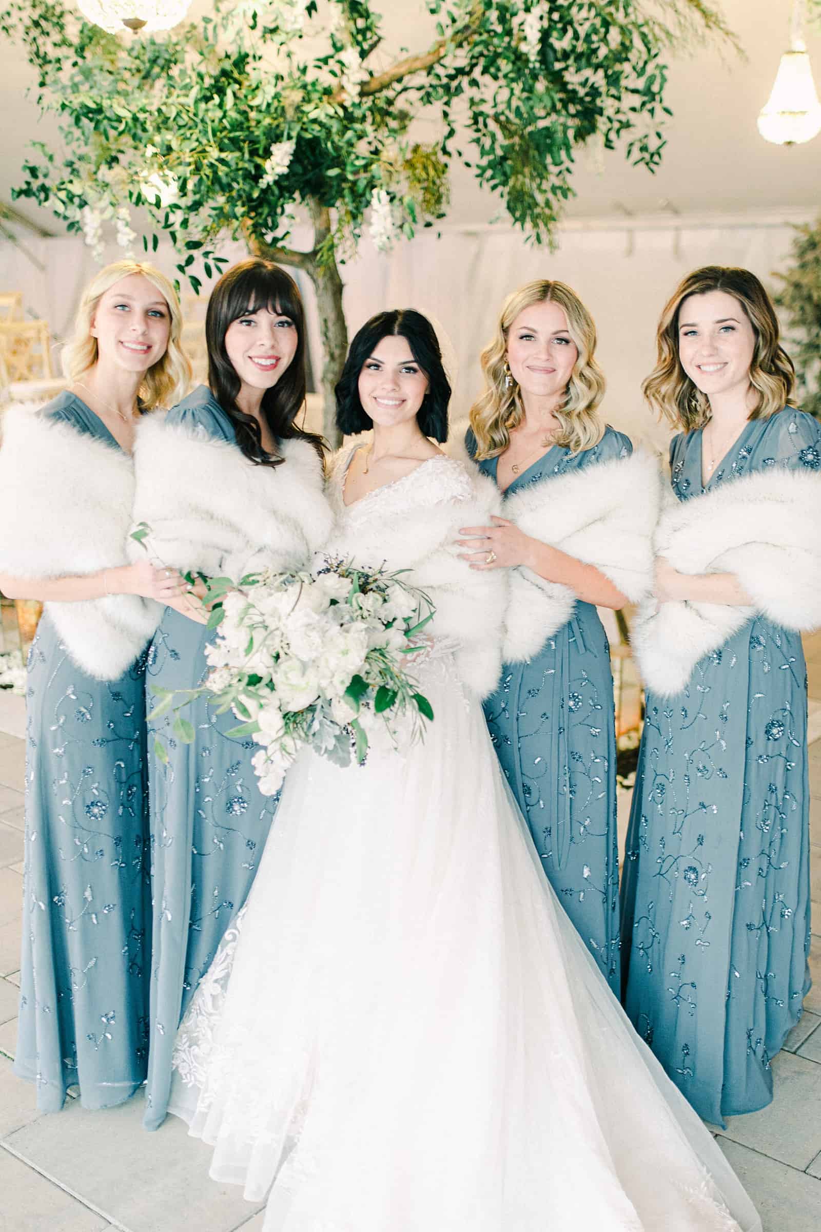 Winter wedding bride with bridesmaids, blue beaded bridesmaids dresses with white fur stoles, white flower bouquets