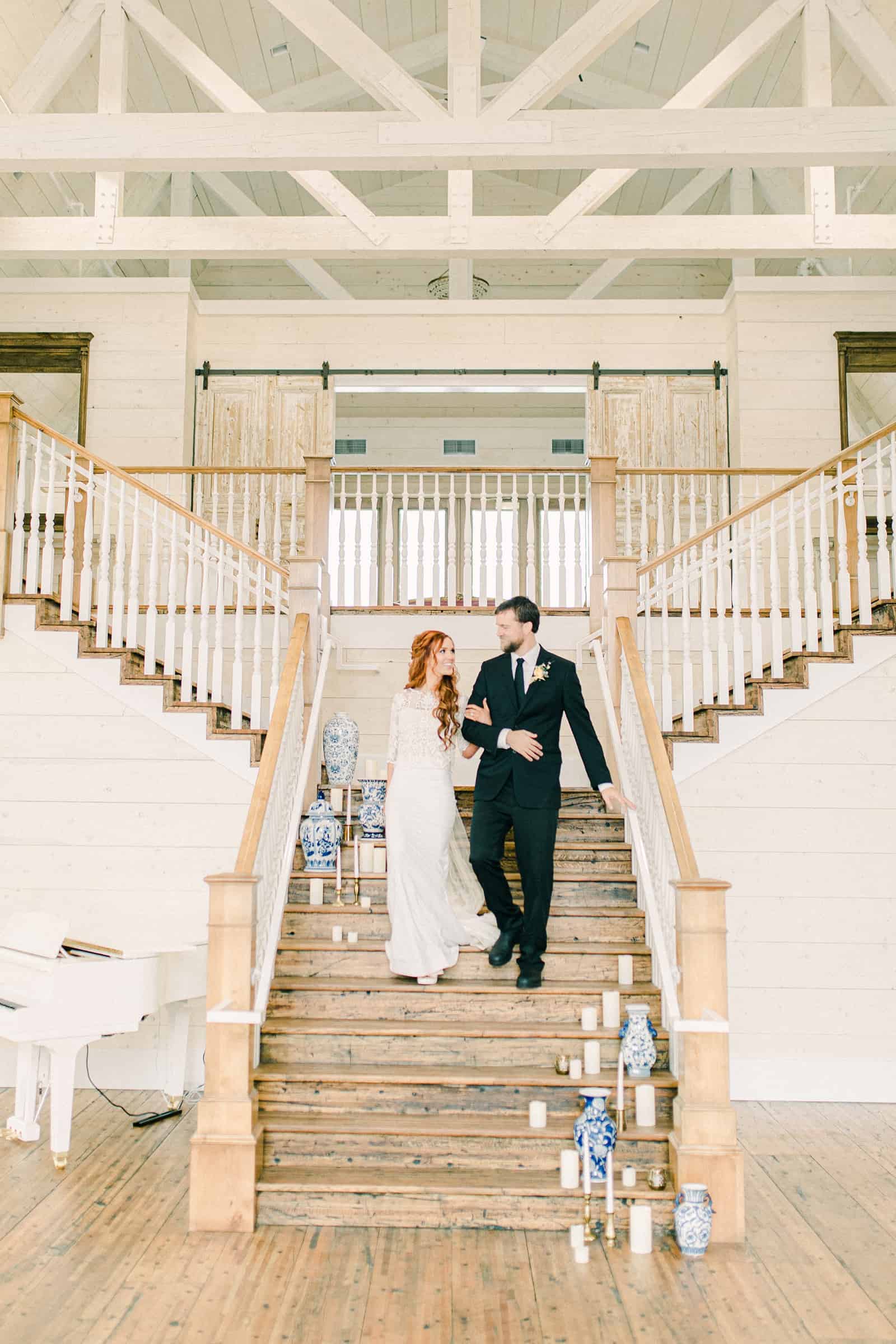 Bride and groom walk down staircase at Walker Farms, Utah white barn modern wedding venue