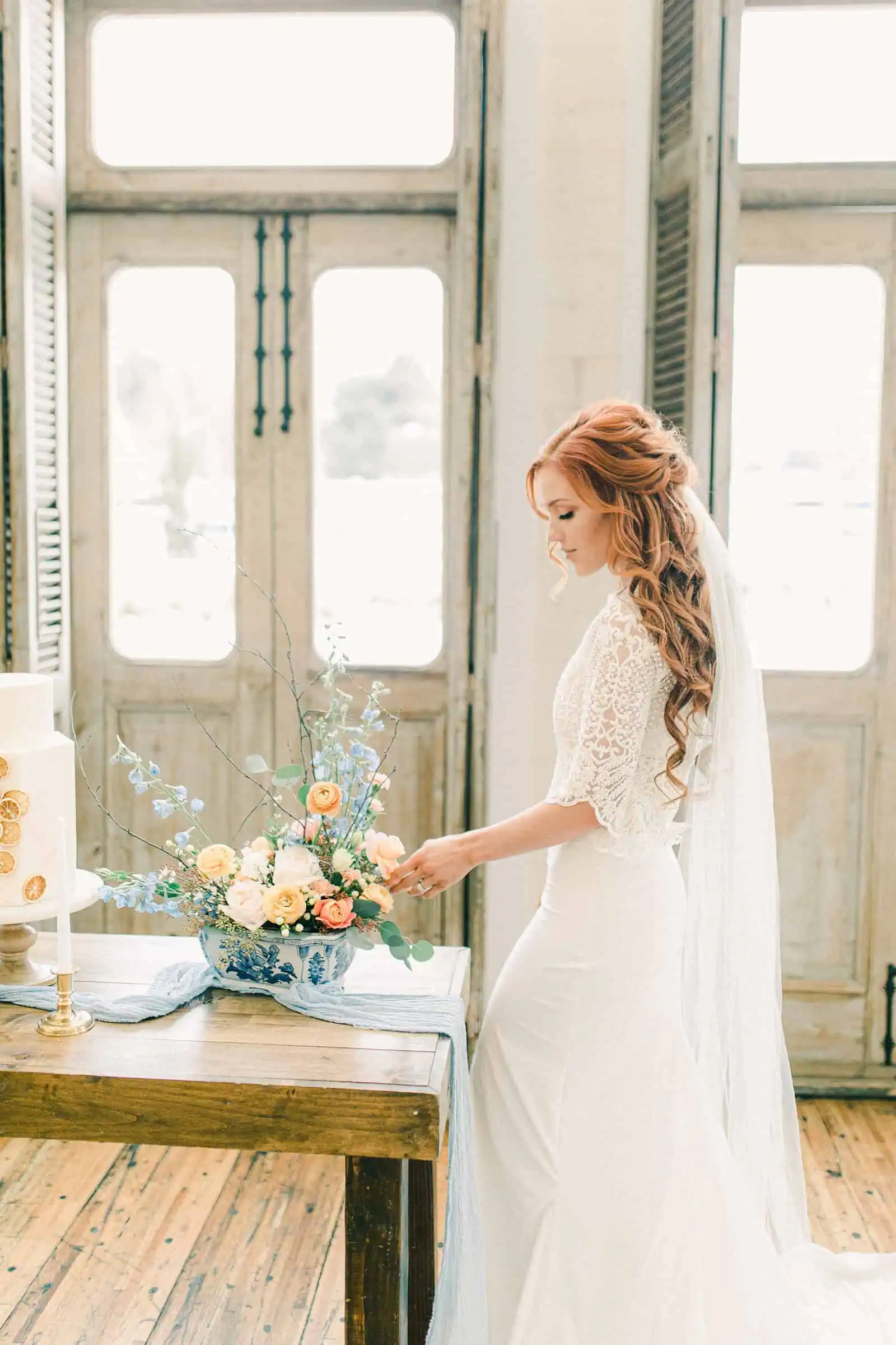 Bride with red hair wearing three quarter length sleeve lace wedding dress and veil, pastel wedding colors, spring wedding centerpiece and small simple wedding cake with oranges