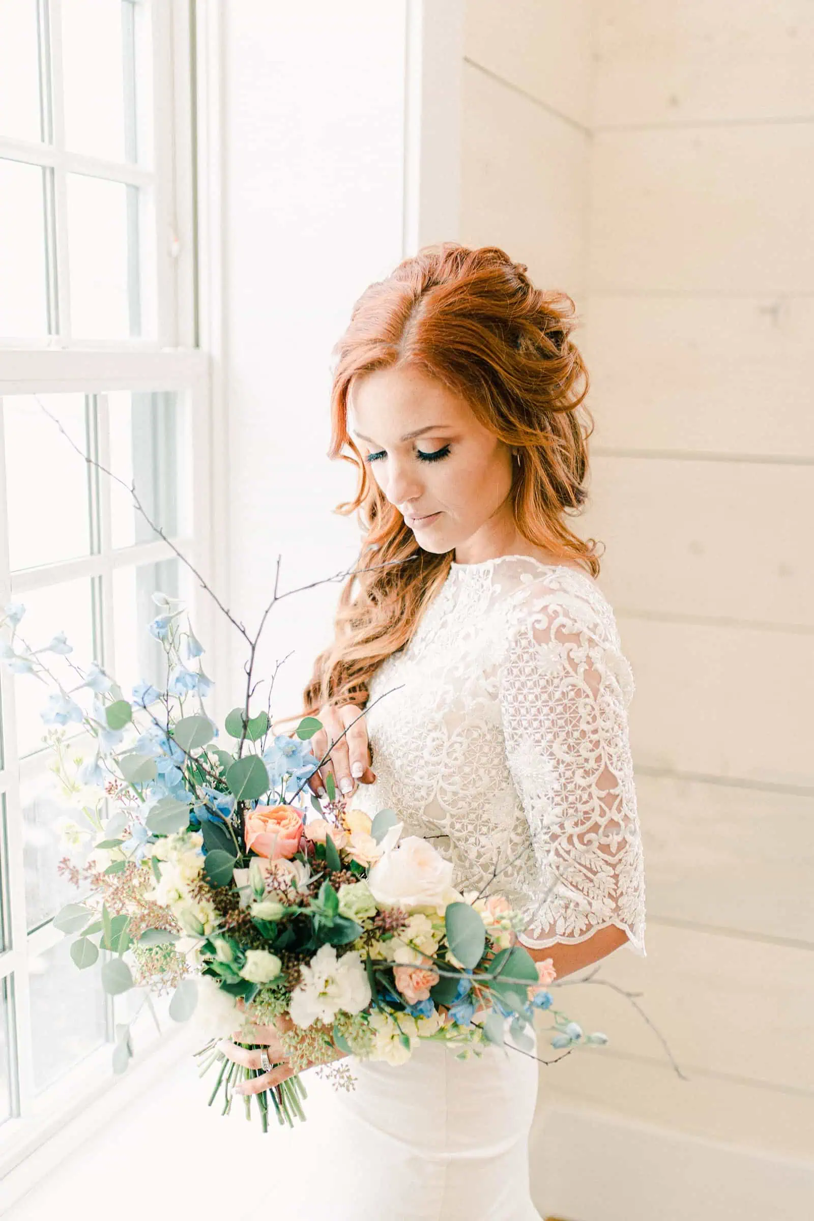 Bride with long lace sleeves holding wedding bouquet with pastel colors, blue, pink, orange, peach flowers