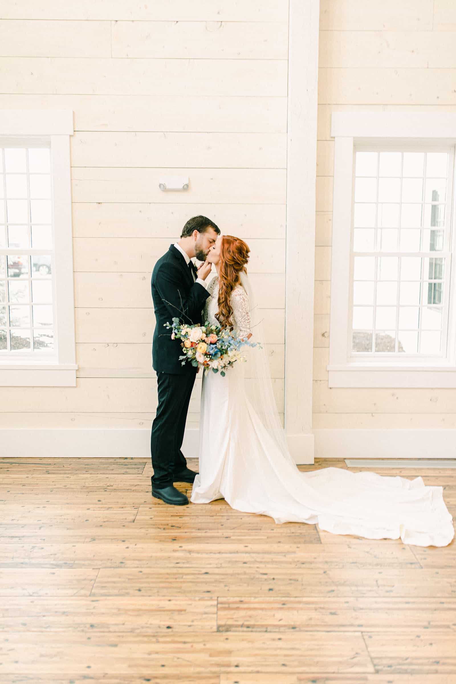 Bride and groom first kiss, white barn wedding venue