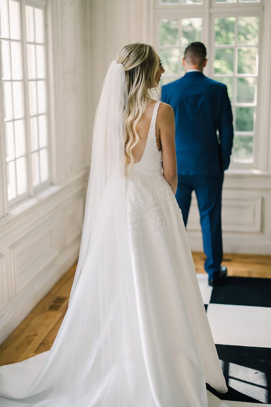 Bride in a white wedding gown with long veil, groom in a blue suit.
