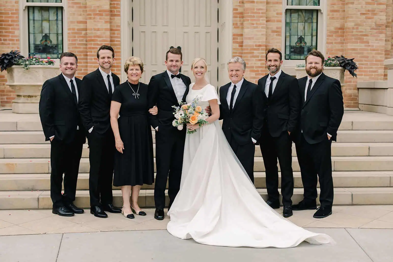 Wedding party outside historic building, bride and groom with family and friends.
