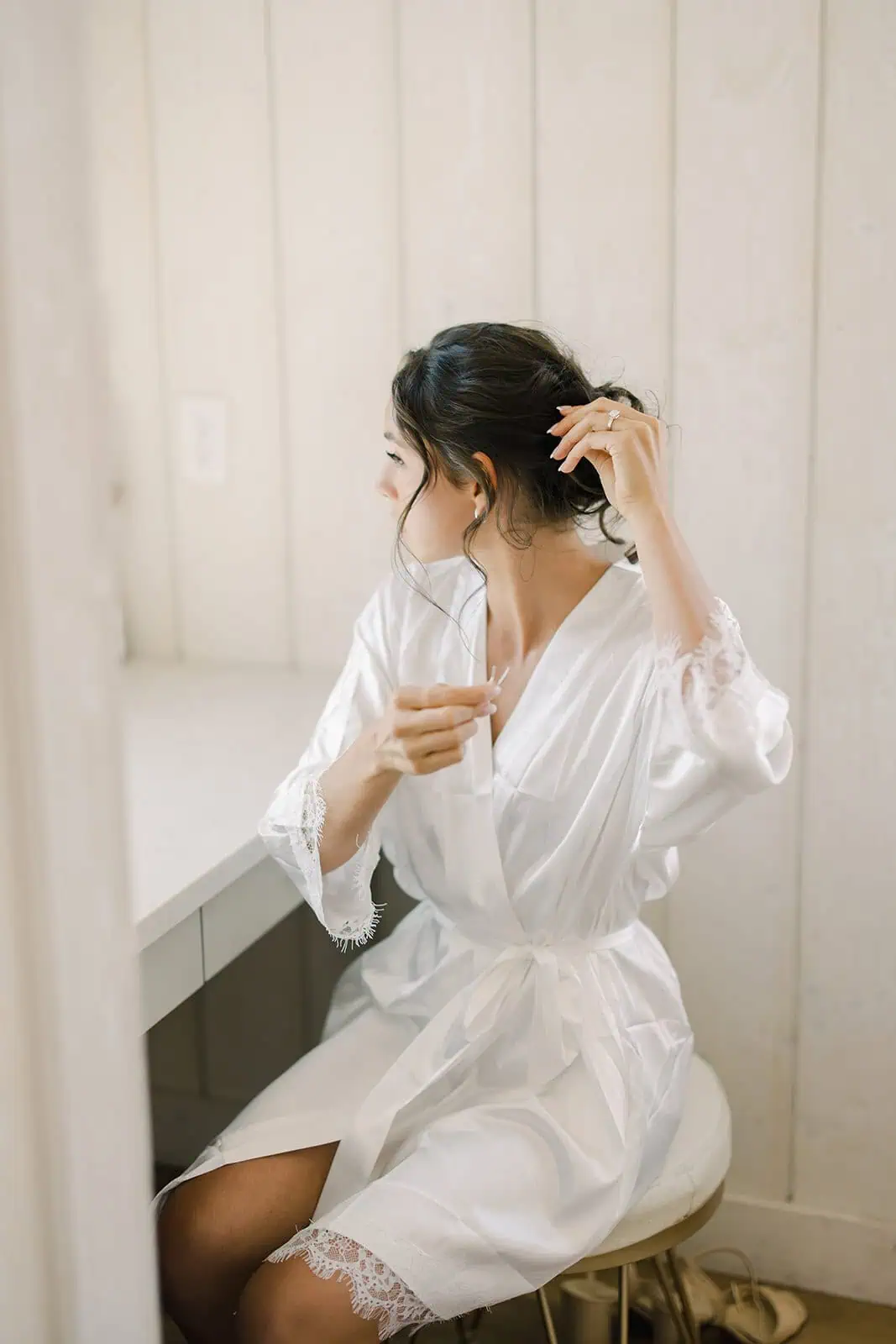 Woman in white robe adjusting her hair in a bright, cozy room.