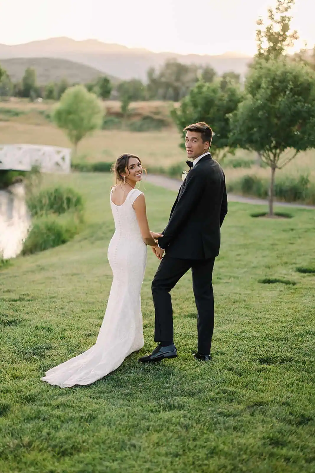 Elegant wedding couple holding hands outdoors at sunset.