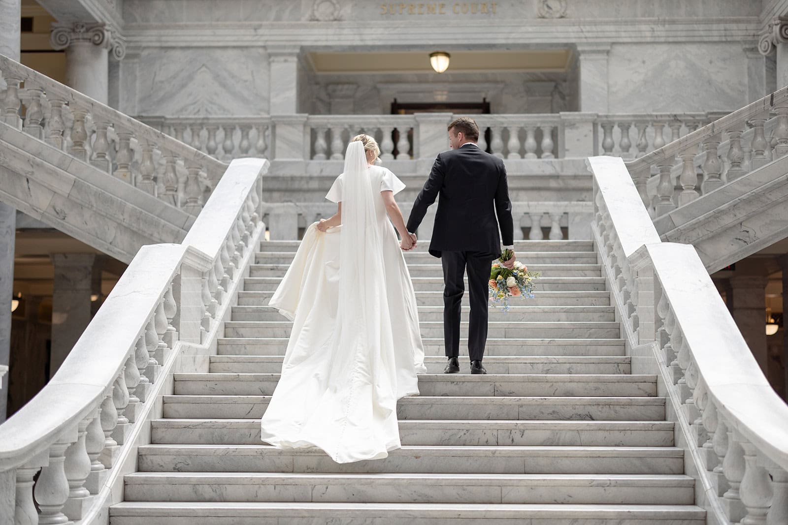 Elegant bride and groom ascending marble staircase.