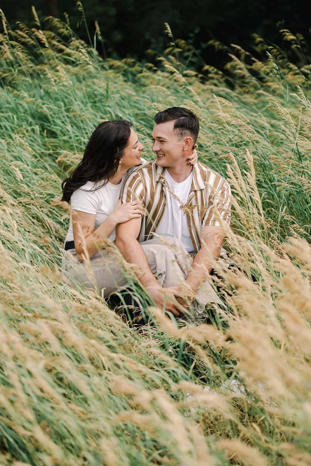 Romantic couple sitting in a lush grassy field, enjoying a peaceful moment together outdoors.